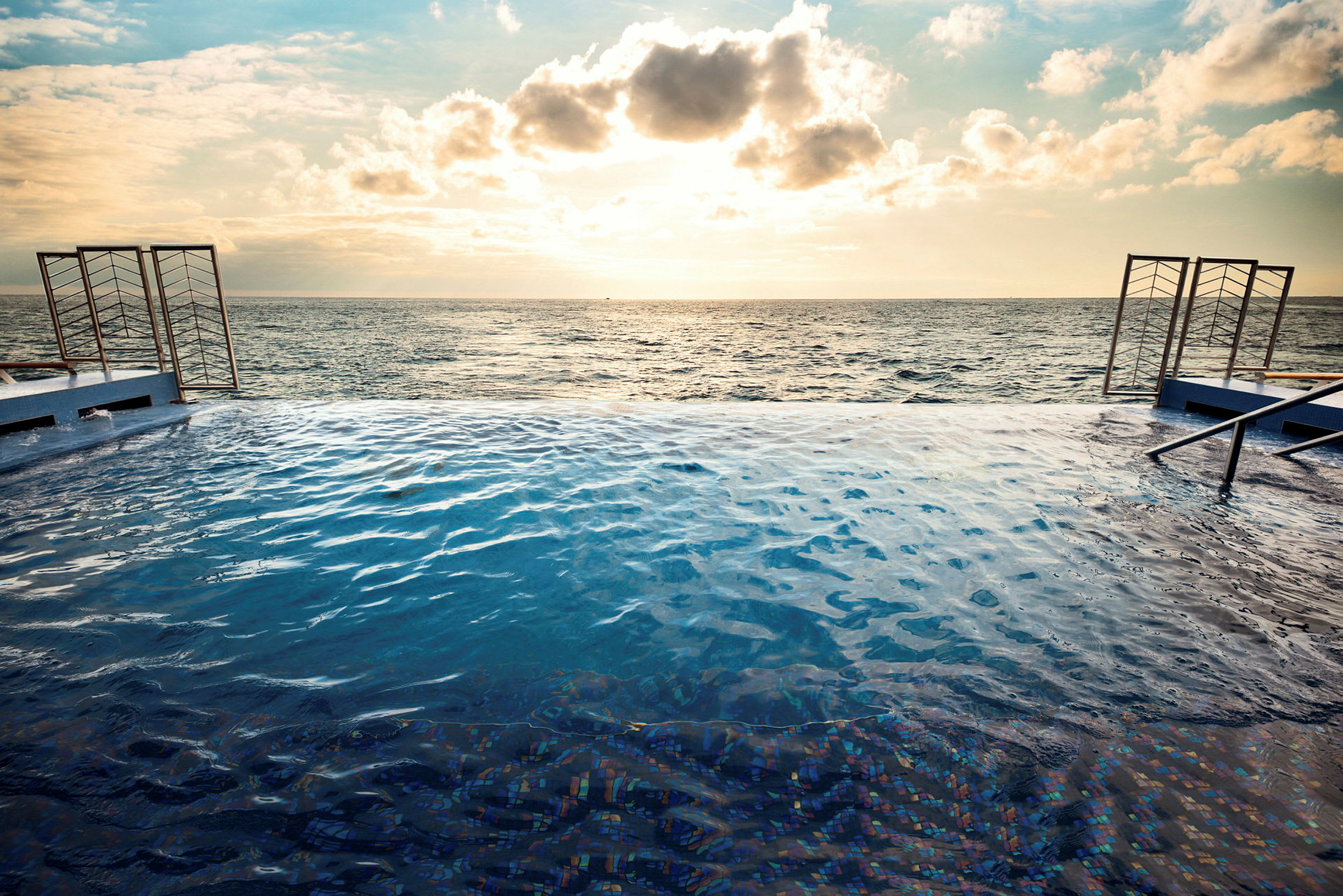 En infinitypool vid havet med solnedgång och moln på himmelen. (AI-genererad text)