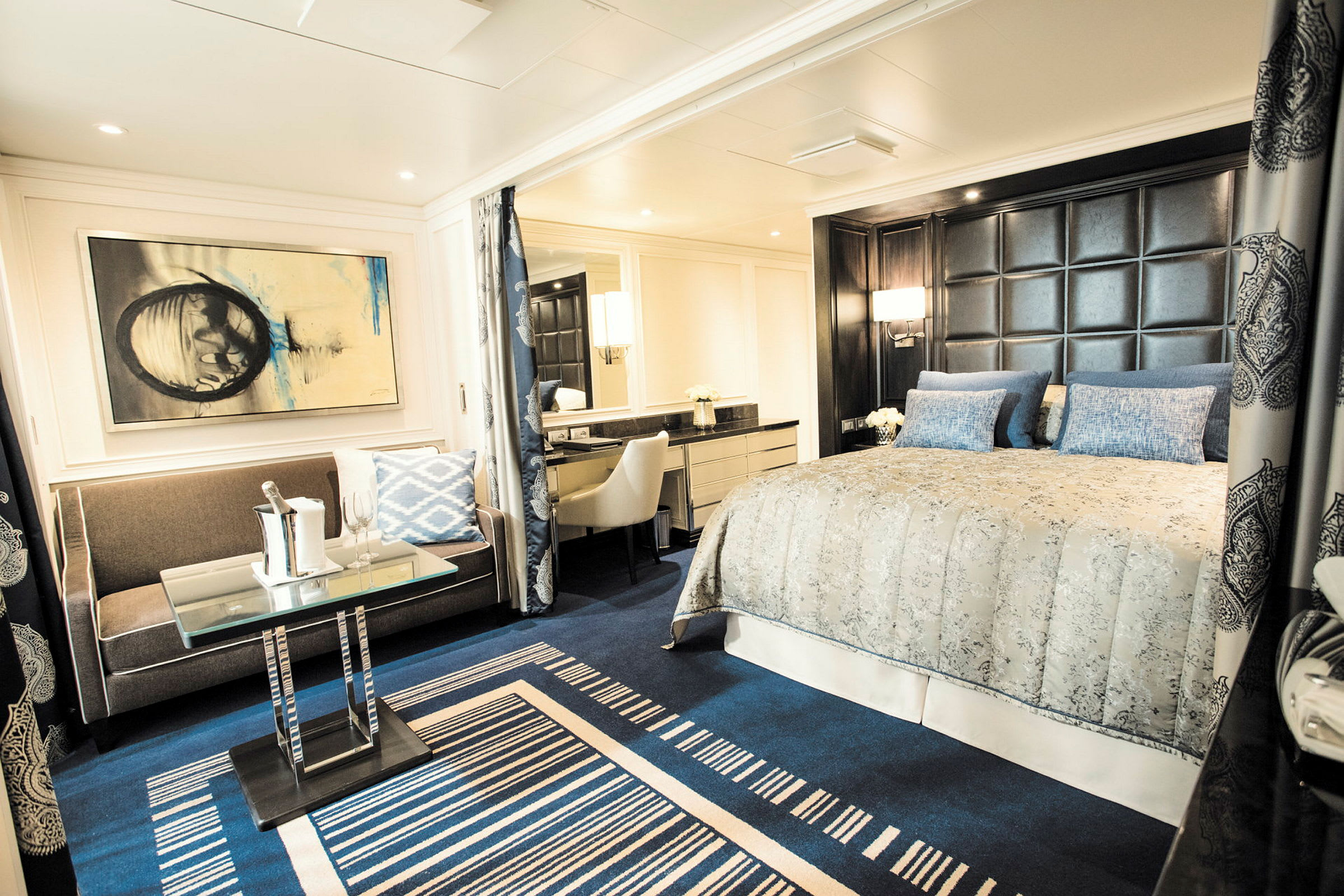 Ett elegant hotellrum med blå mattor, dubbelsäng, soffa och modern inredning. (AI-genererad text)