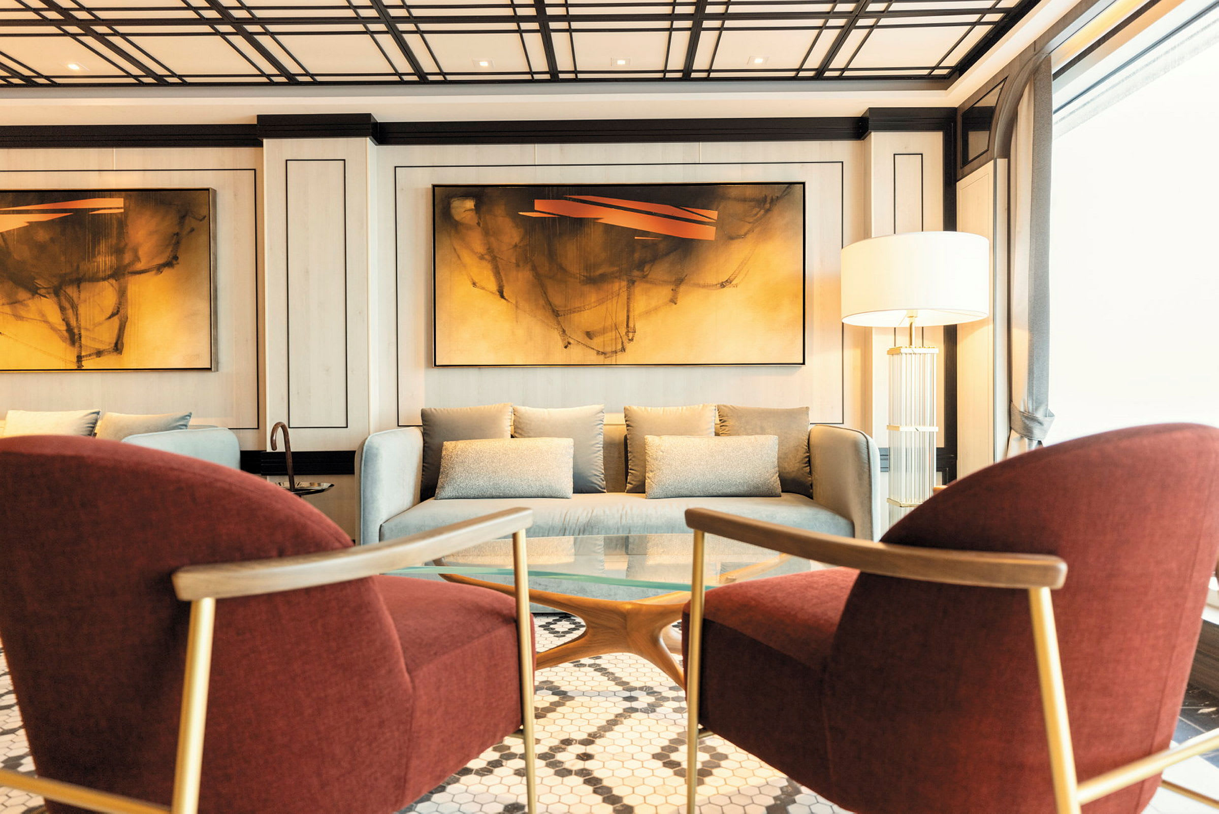 En modern hotellobby med sittgrupp, bestående av två röda fåtöljer, en soffa och en lampett. (AI-genererad text)