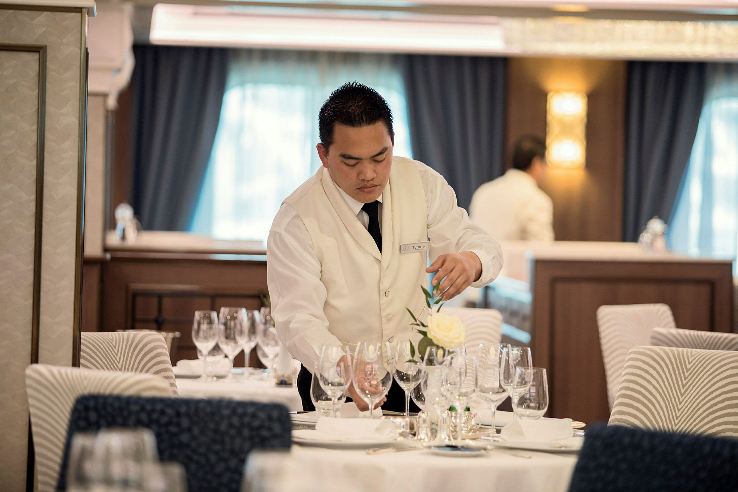 En servitör arrangerar glas och dekor på ett dukat bord i en restaurang. (AI-genererad text)