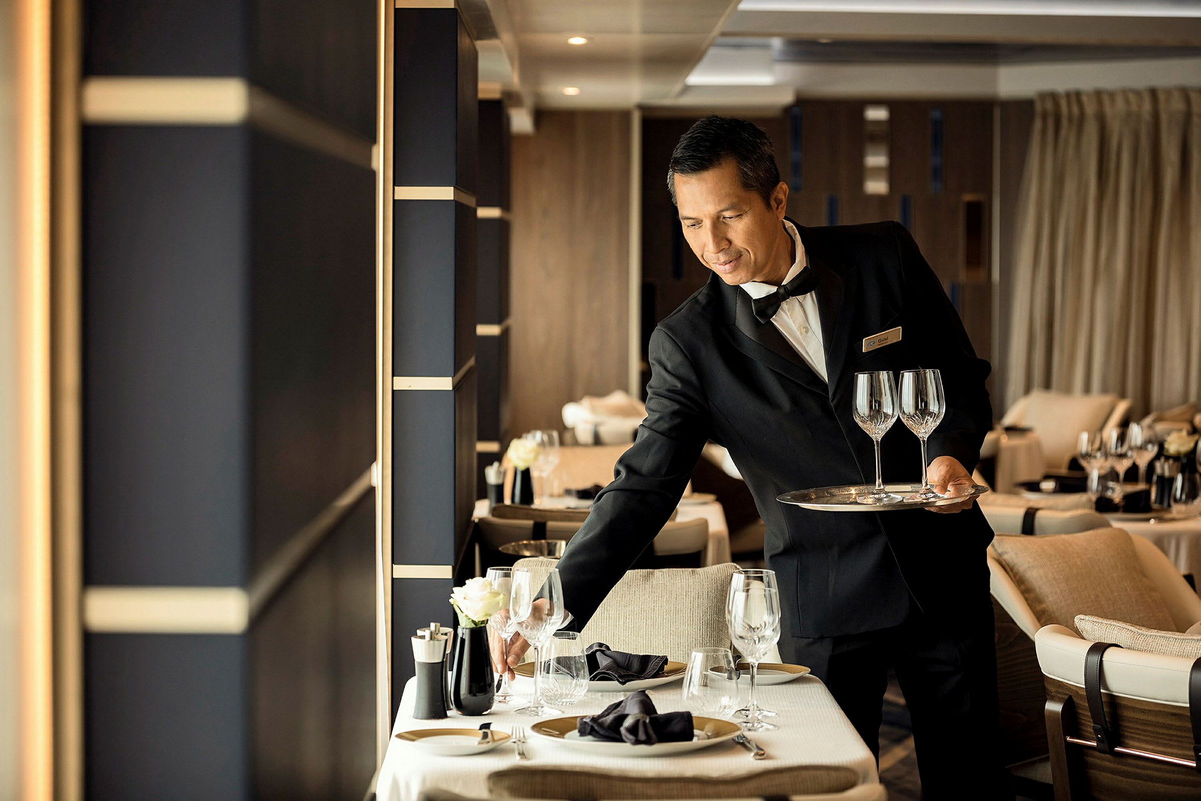 Servitör arrangerar glas på ett dukat bord i restaurang. (AI-genererad text)