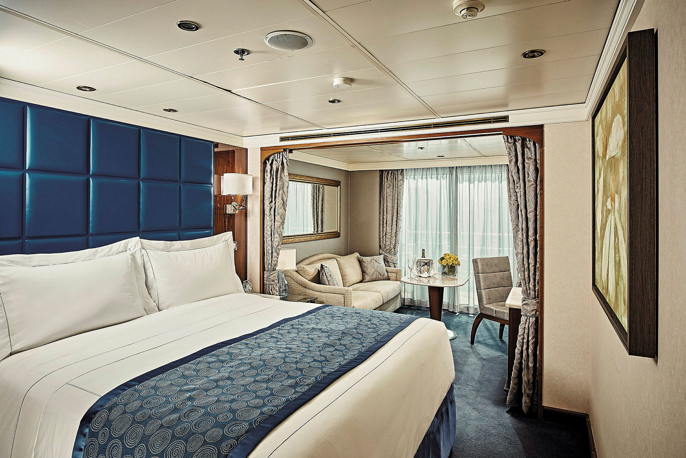 Ett hotellrum med en stor säng, sittgrupp och ett bord vid ett fönster. (AI-genererad text)