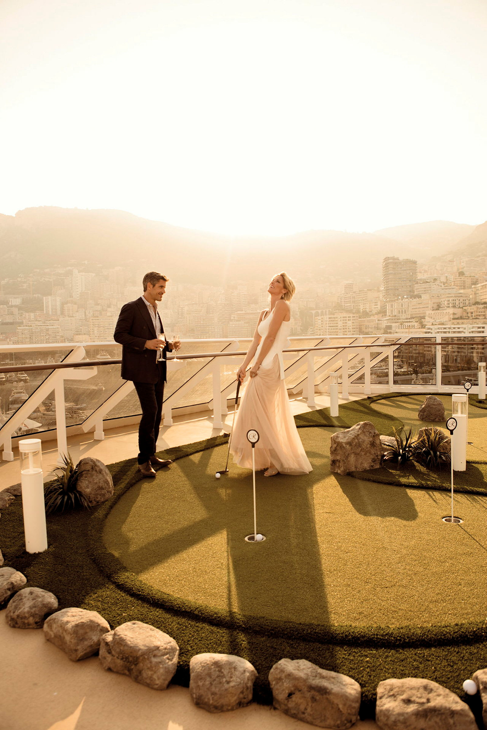 En duo står på ett mini-golfområde på en terrass med utsikt över en stad i solnedgången. (AI-genererad text)