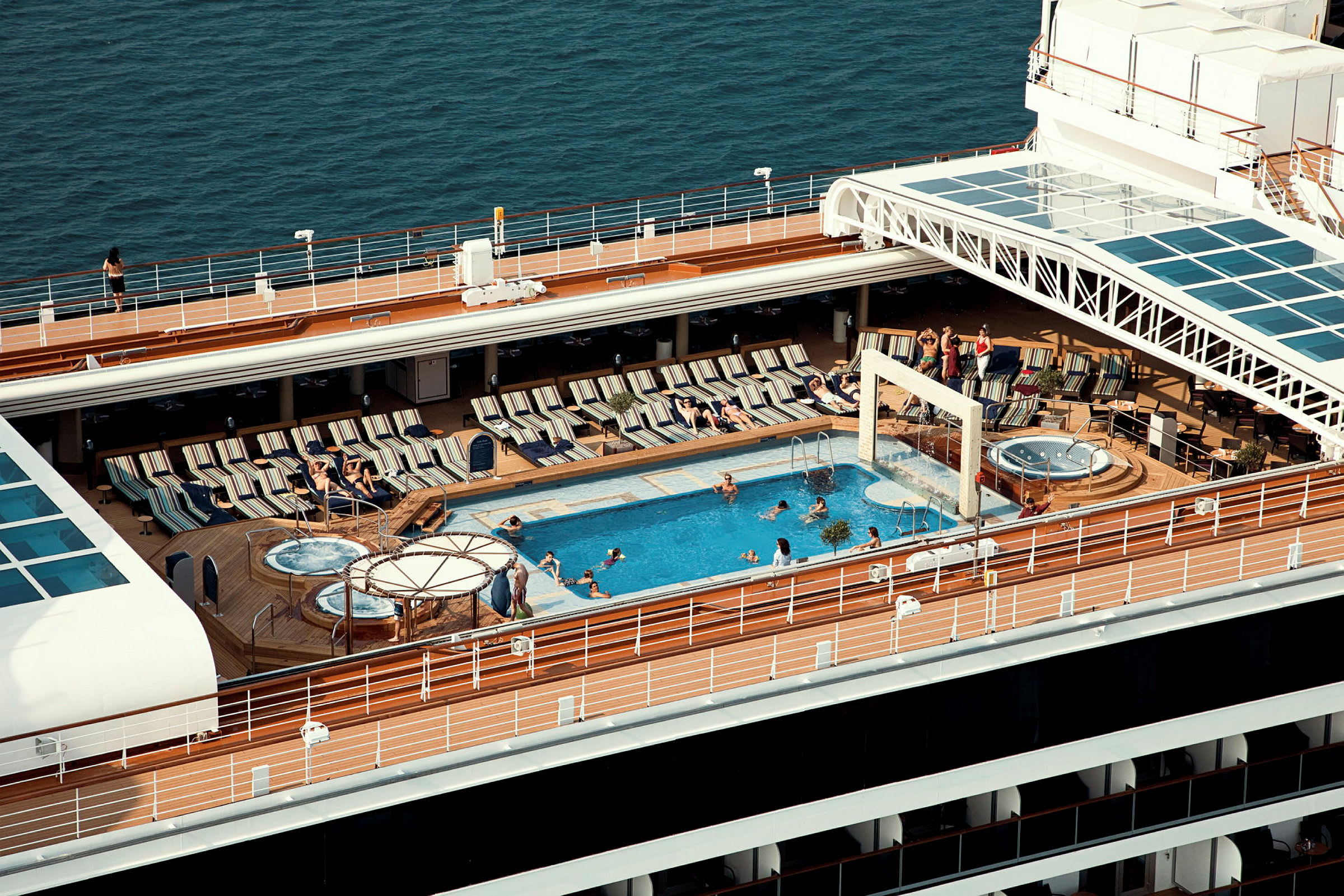 Ett fartygsdäck med en pool, solstolar och personer som njuter av solen. (AI-genererad text)