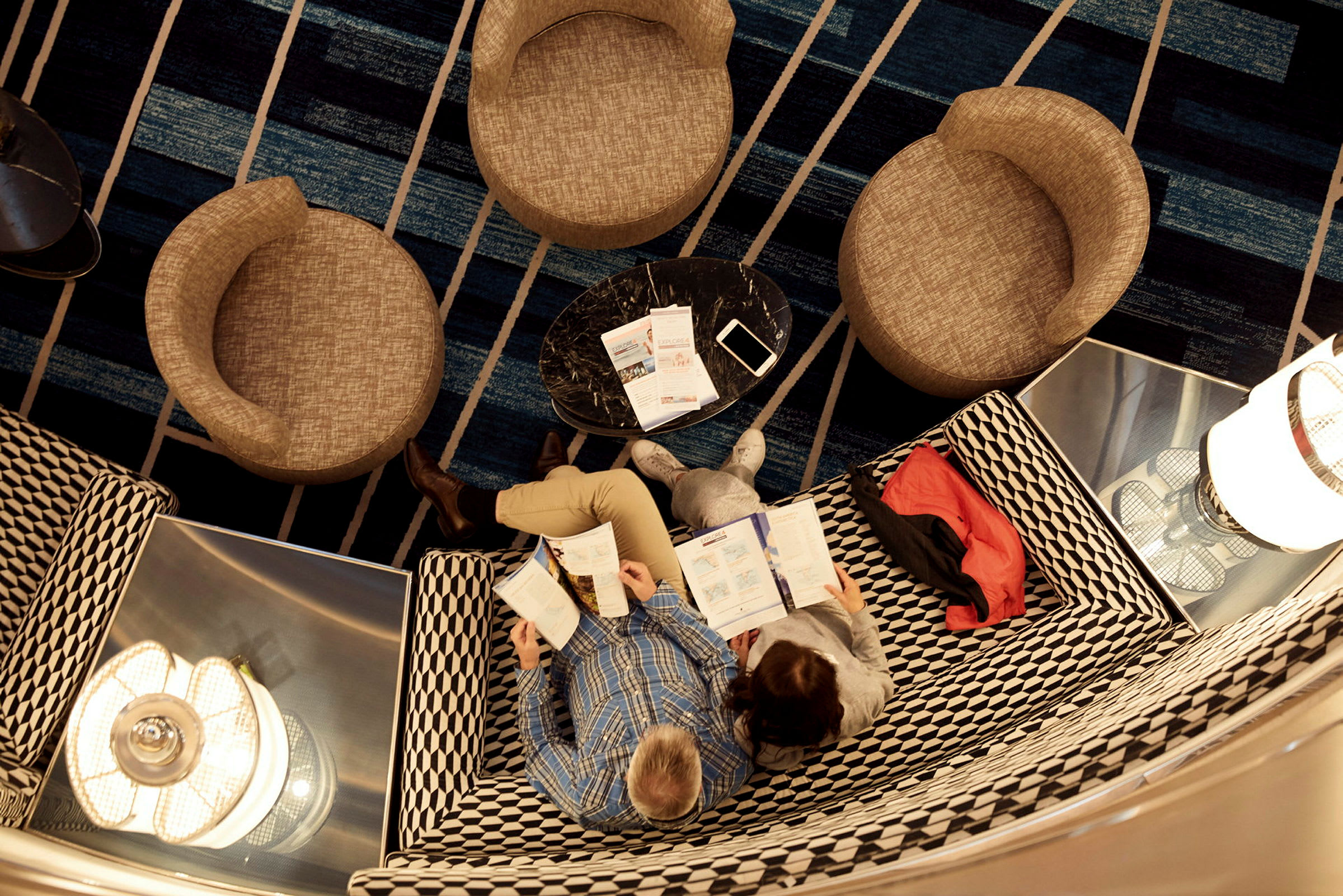 Två personer läser broschyrer vid ett bord i en lounge. (AI-genererad text)