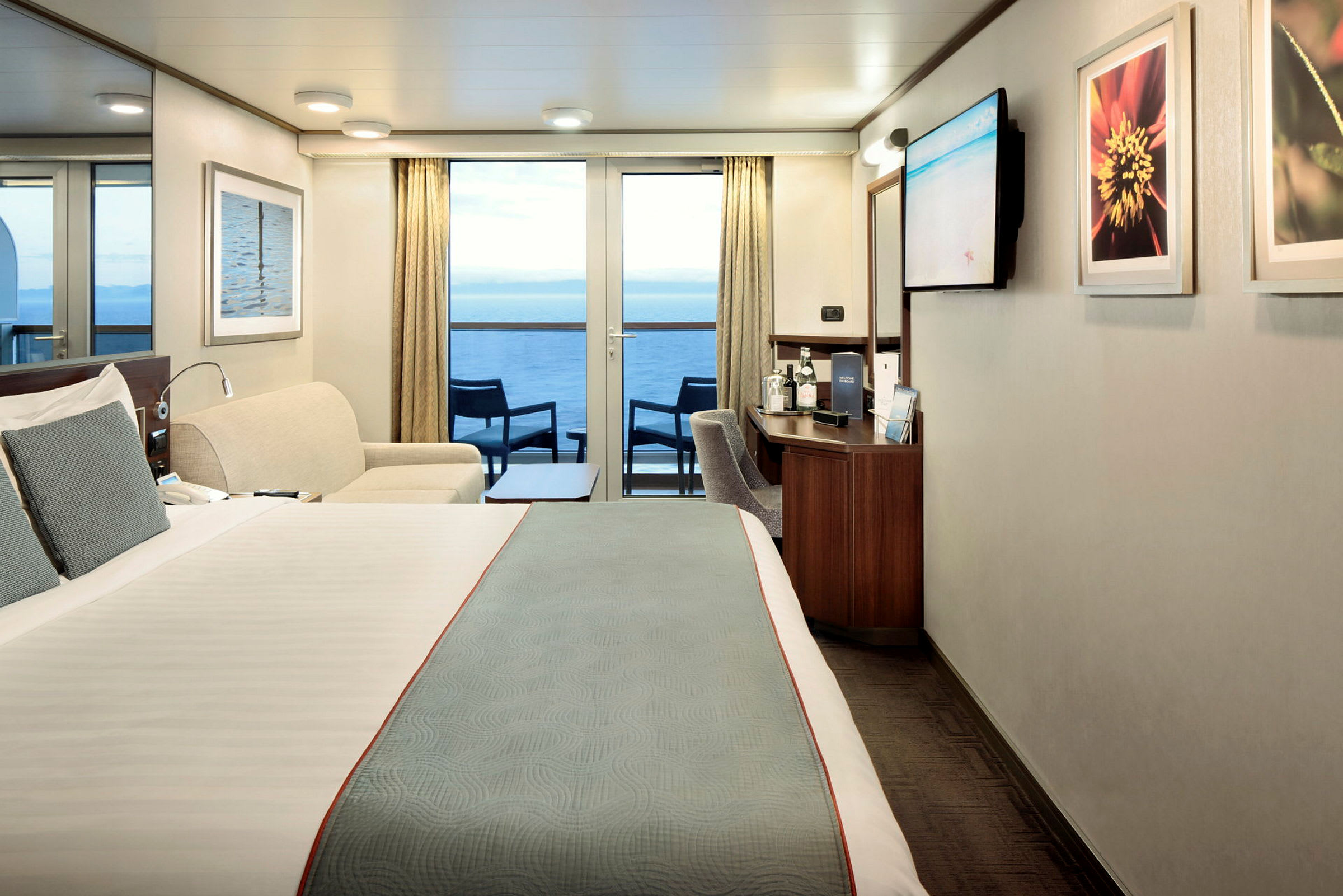 Hotellrum med en dubbelsäng, sittgrupp och balkong med utsikt över havet. (AI-genererad text)