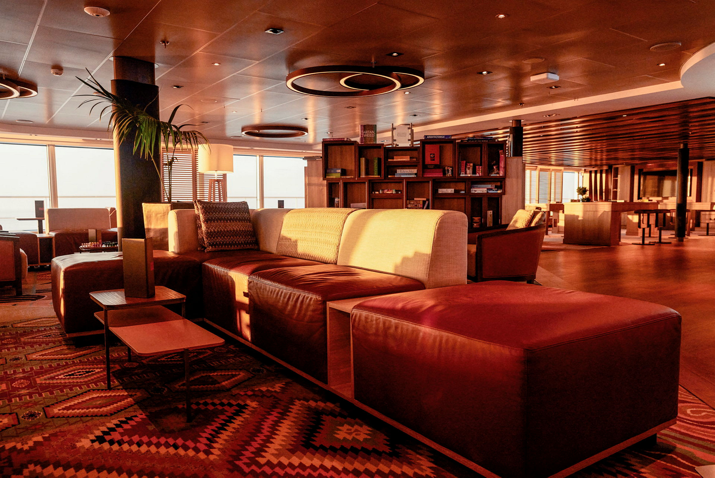 En elegant inredd gemensam lounge med soffor, bord och bokhyllor, belyst av varmt solljus. (AI-genererad text)