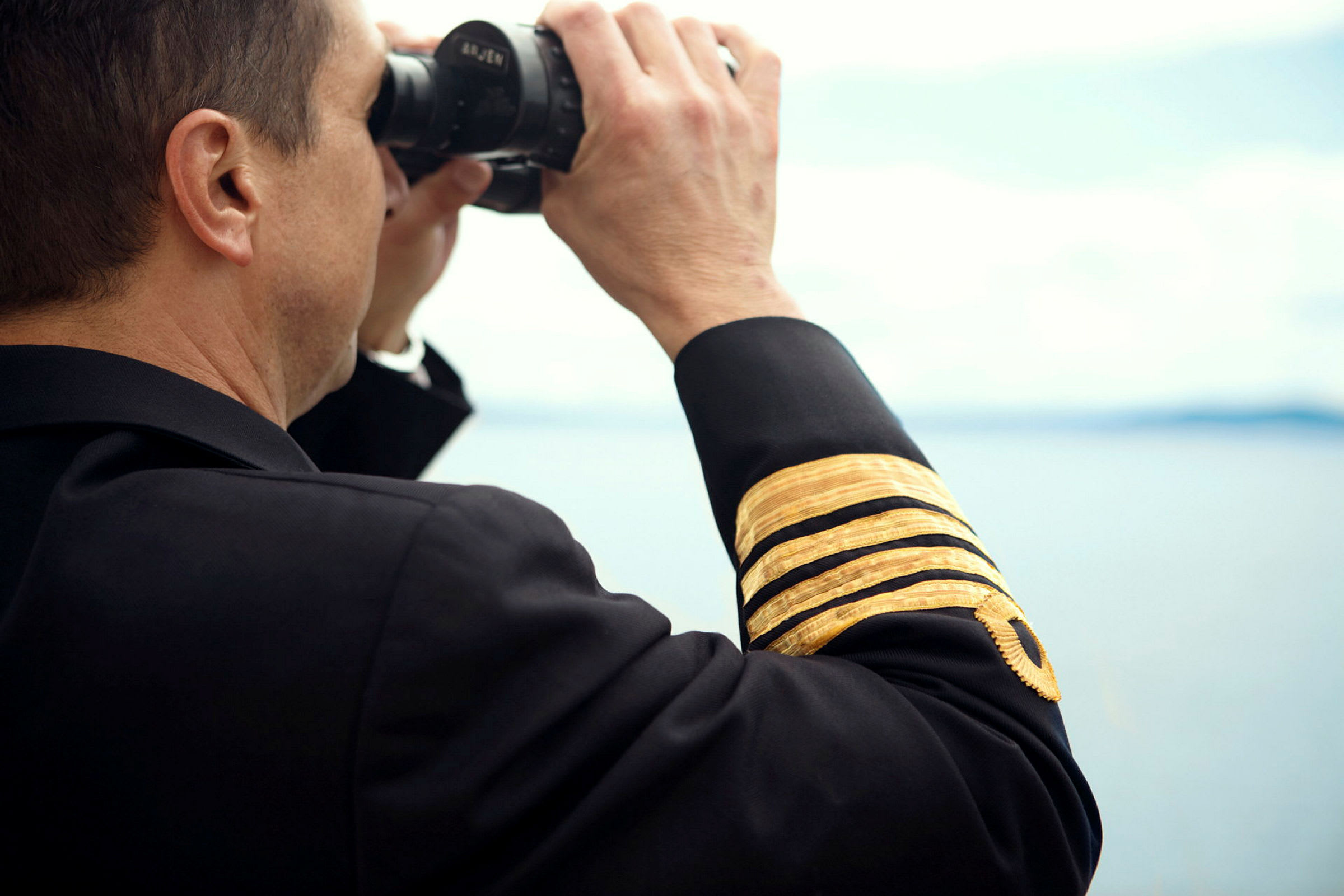 En person i uniform håller i en kikare och tittar mot horisonten. (AI-genererad text)