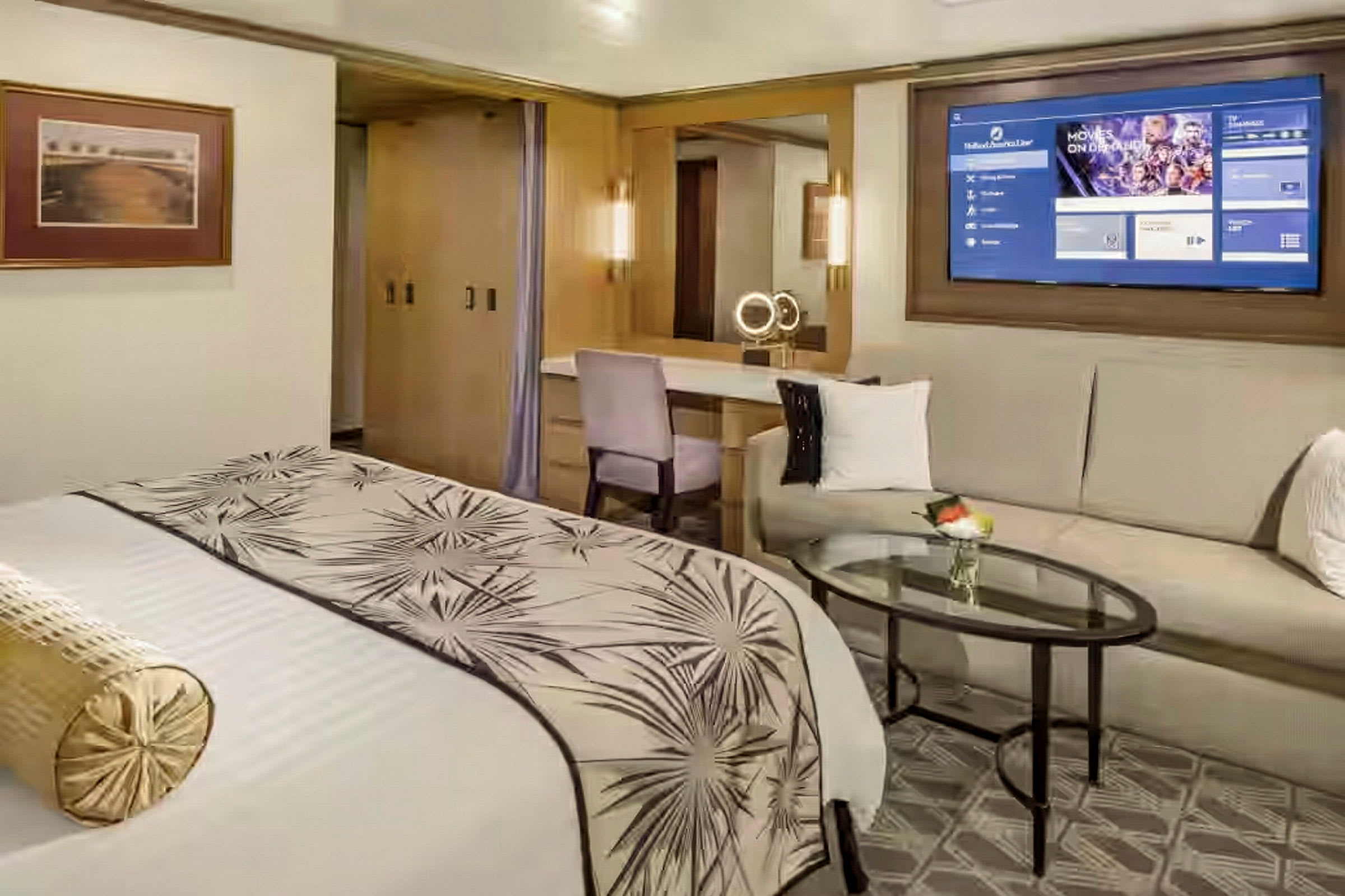 Ett elegant hotellrum med en stor säng, dekorerat med ett mönstrat överkast, en soffa och ett soffbord, samt en väggmonterad TV. (AI-genererad text)
