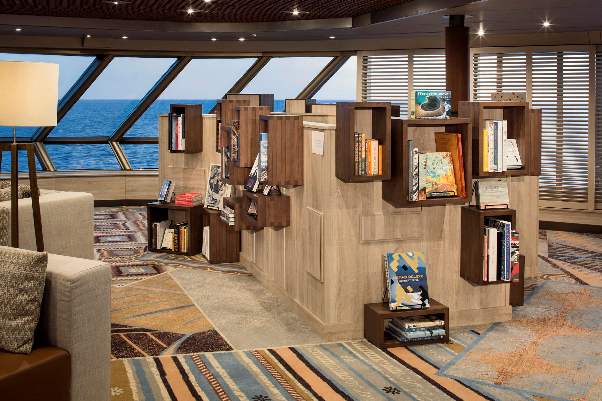 En modern lounge med bokhyllor fyllda med böcker, stora fönster med utsikt över havet och dekorativa detaljer i interiören. (AI-genererad text)
