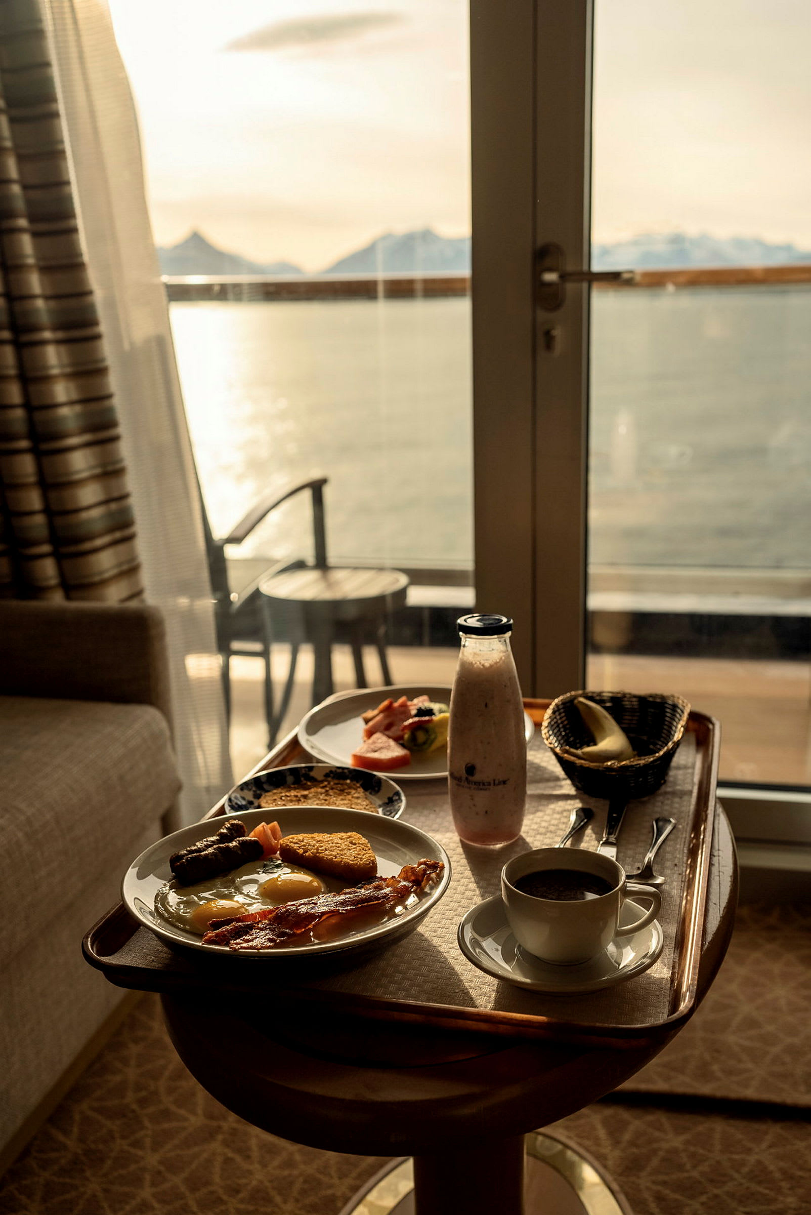 En bricka med frukostmat står på ett bord framför en glasdörr med utsikt över vatten och berg. (AI-genererad text)