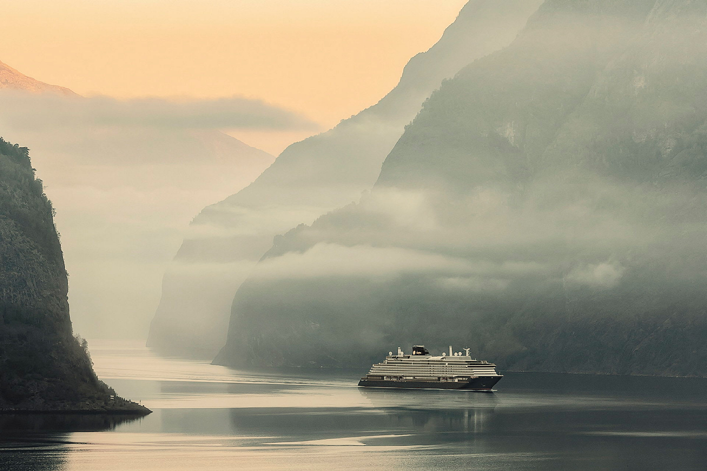 Ett kryssningsfartyg i en dimmig fjordlandskap. (AI-genererad text)