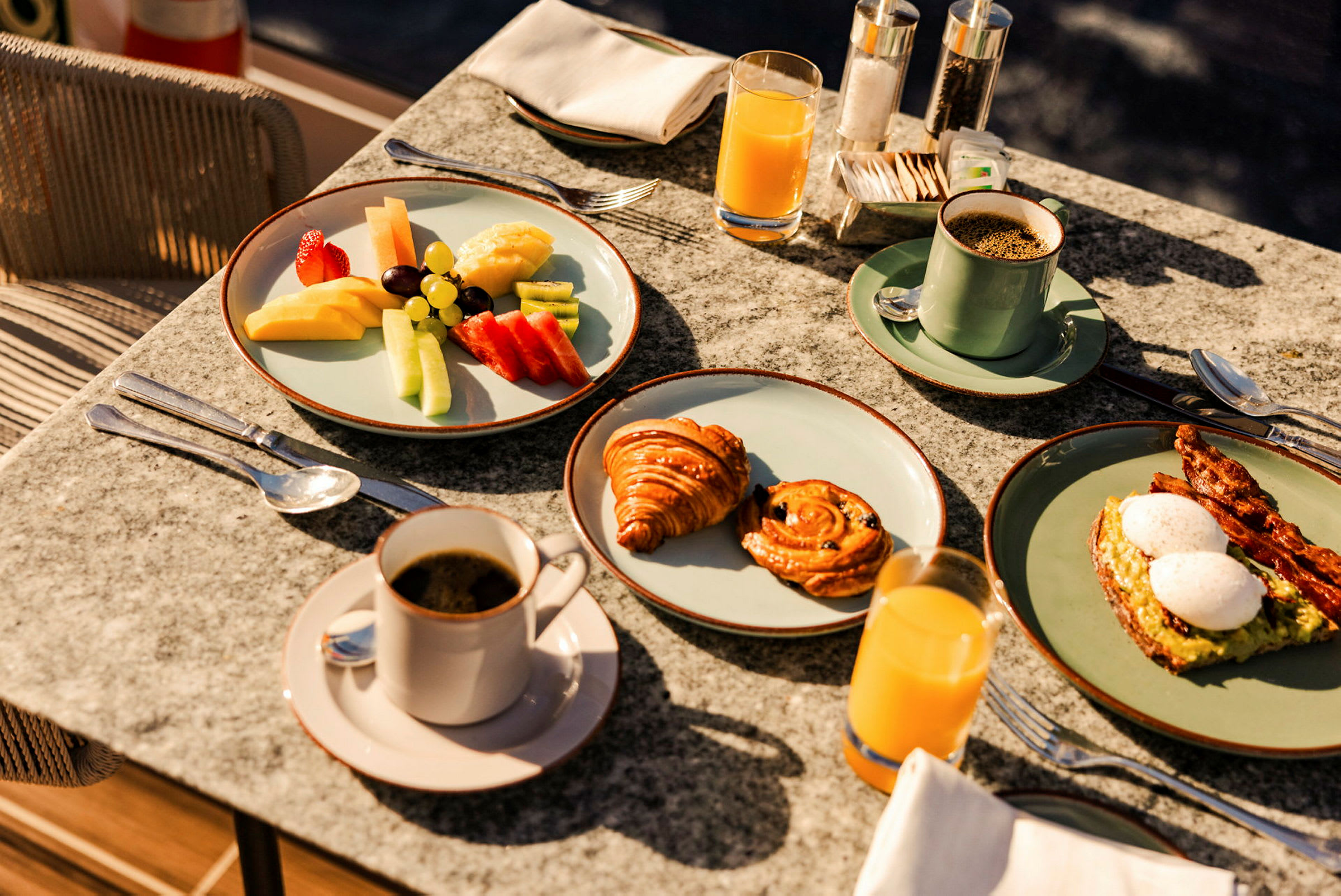 En frukostmåltid med kaffe, juice, frukt, bakverk och ägg med bacon. (AI-genererad text)