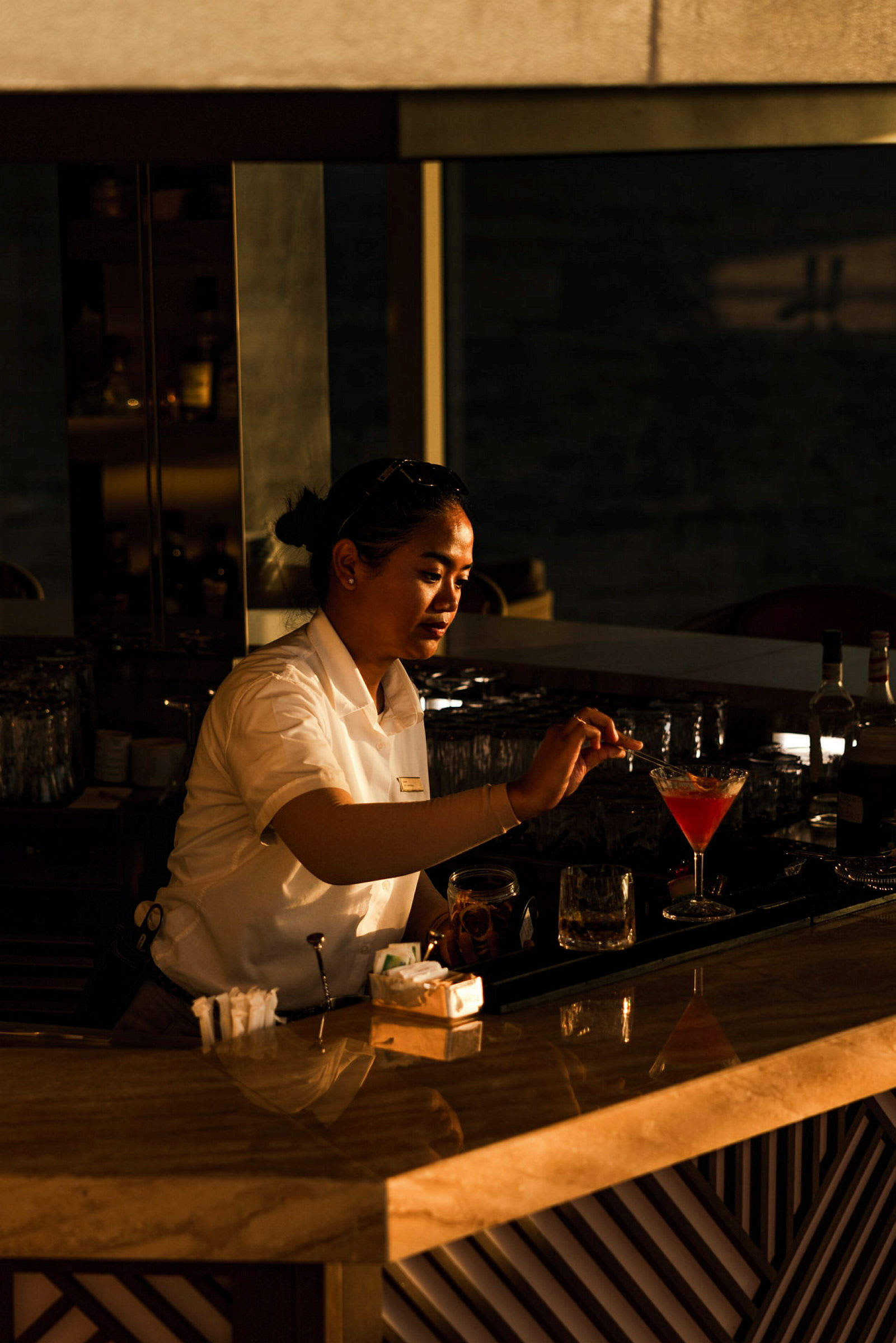 En person i tjänstekläder förbereder en cocktail vid en hotellbar. (AI-genererad text)