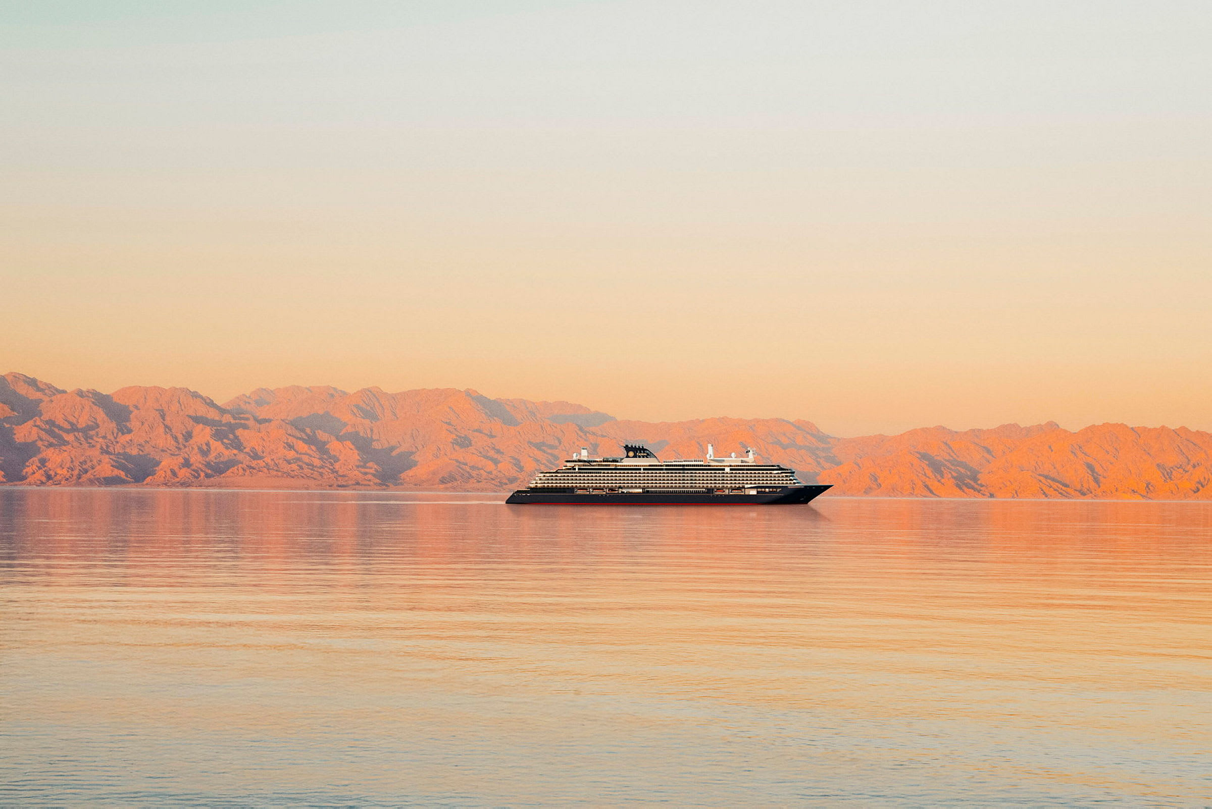 En kryssningsfartyg på ett stilla hav med berg i bakgrunden under solnedgång. (AI-genererad text)
