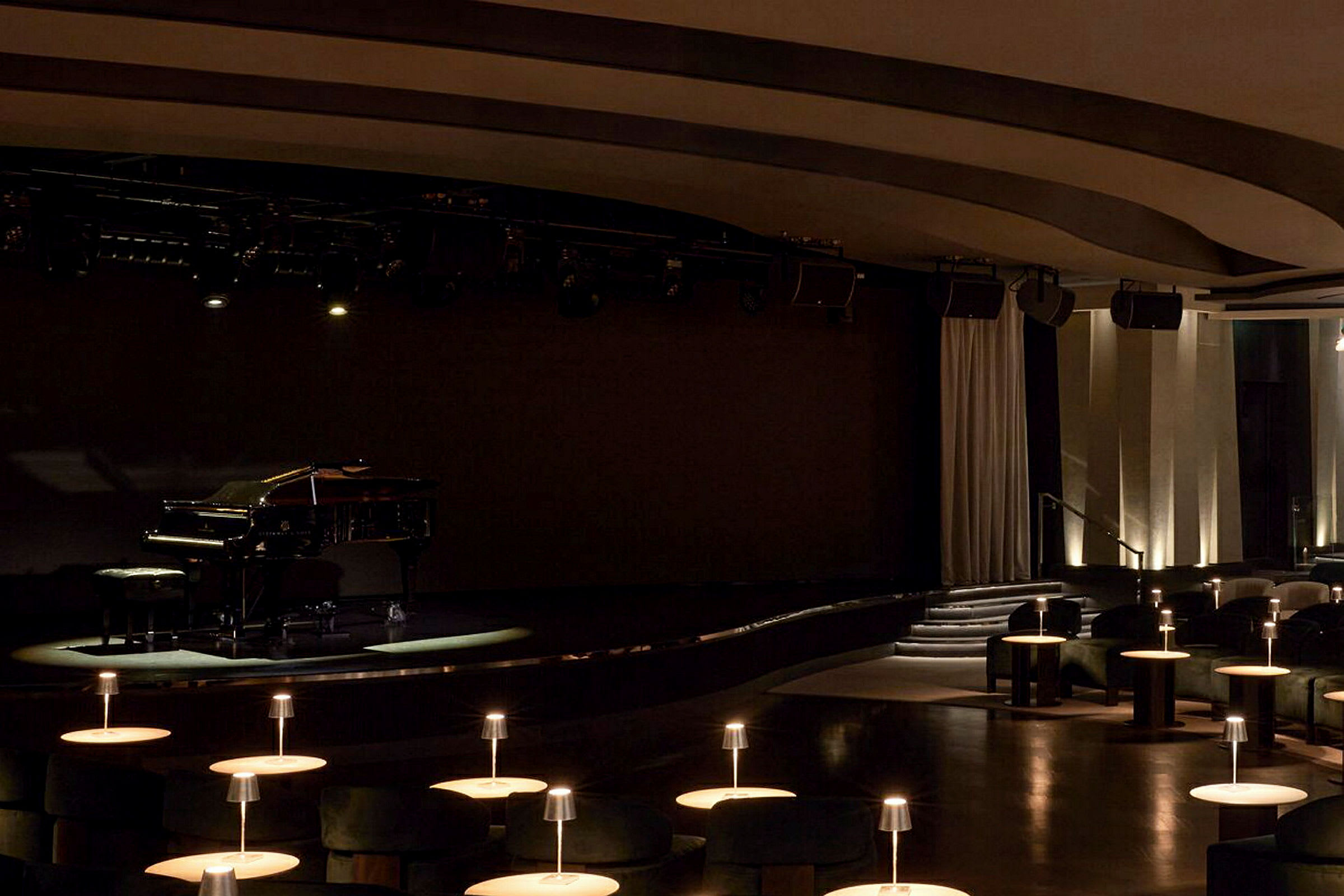 Det är ett piano på en scen, med sittplatser och bord upplysta i förgrunden. (AI-genererad text)