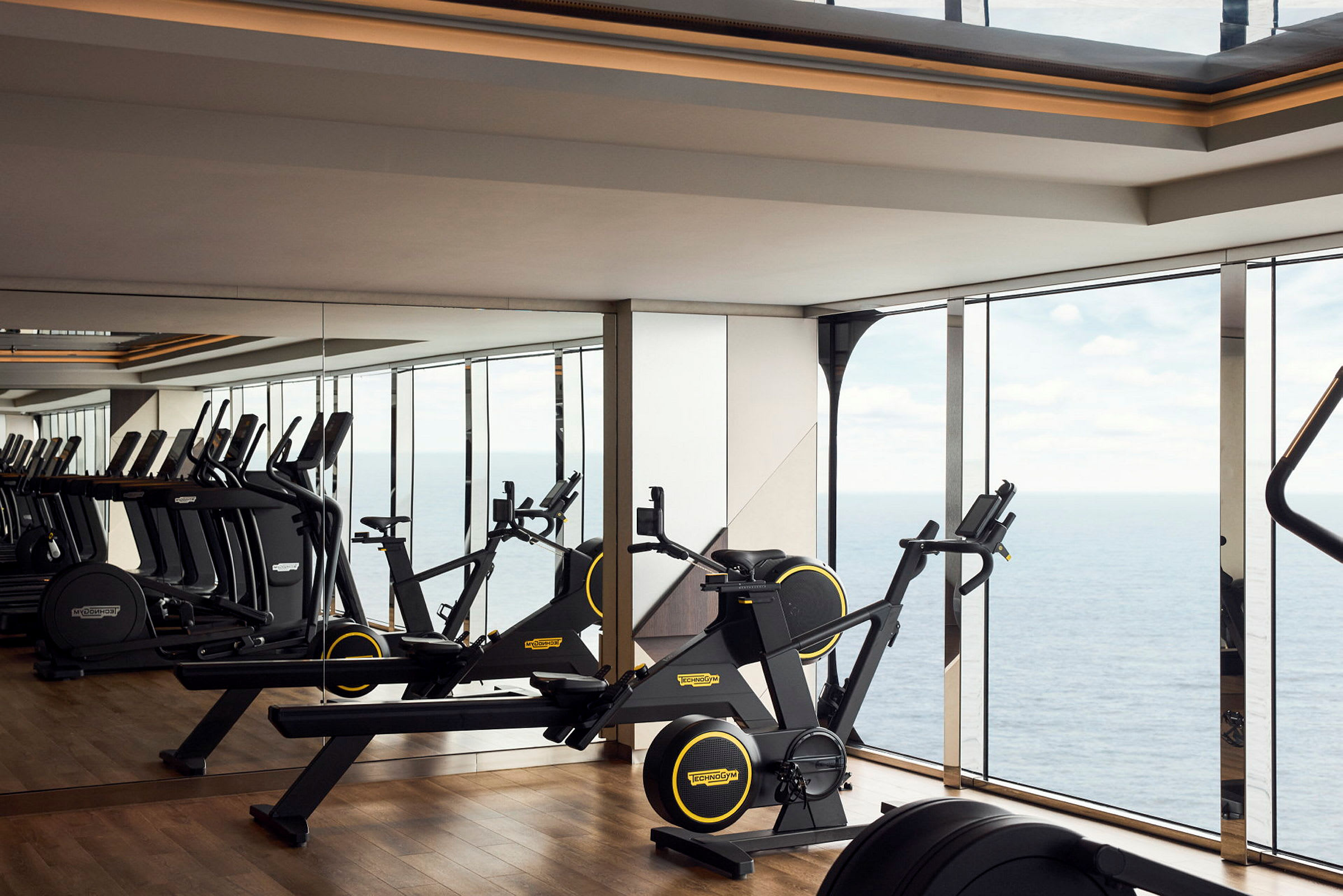Ett gym med träningsmaskiner och spegelväggar samt utsikt över havet. (AI-genererad text)