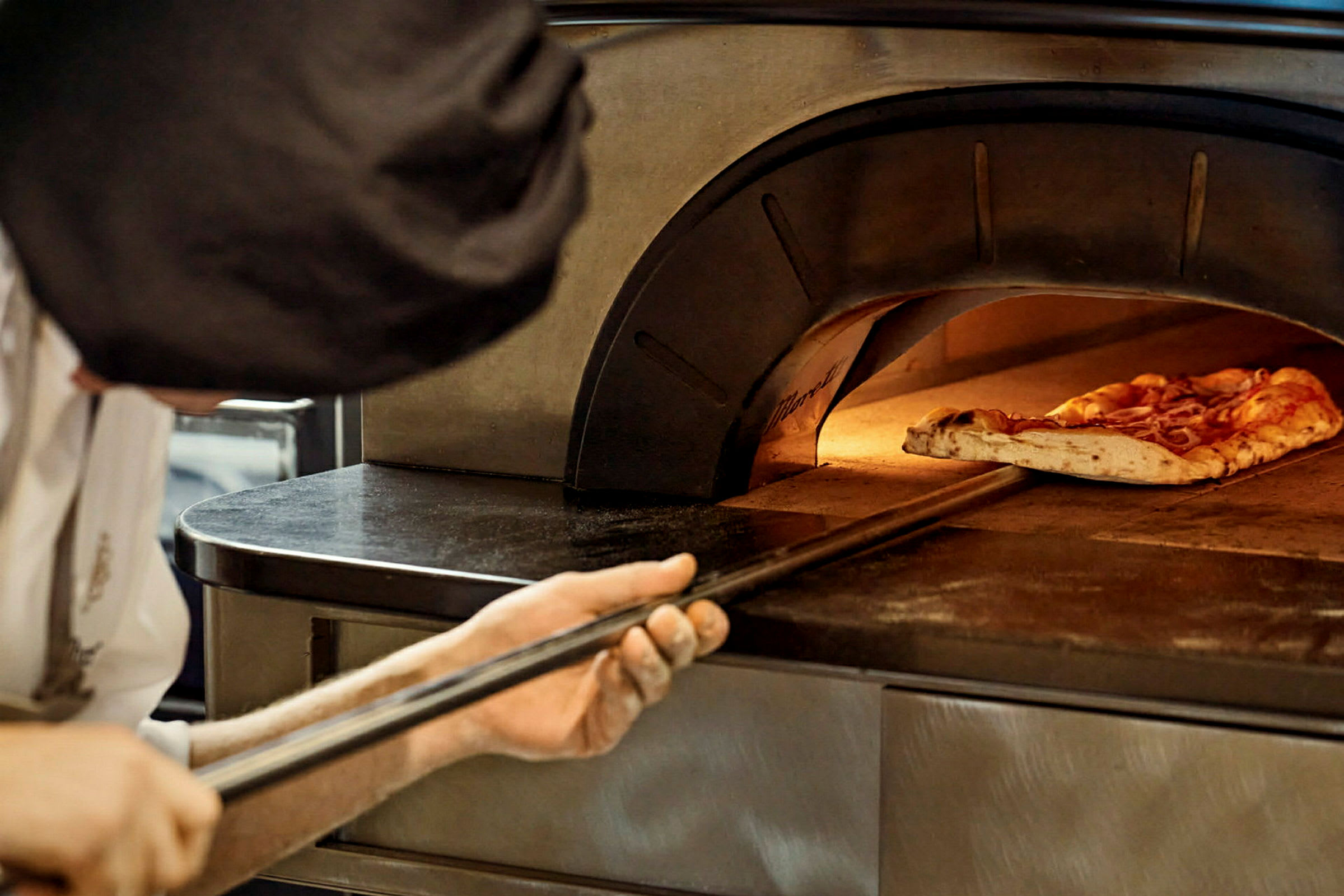 En person skjuter in en pizza i en ugn med en pizzaspade. (AI-genererad text)