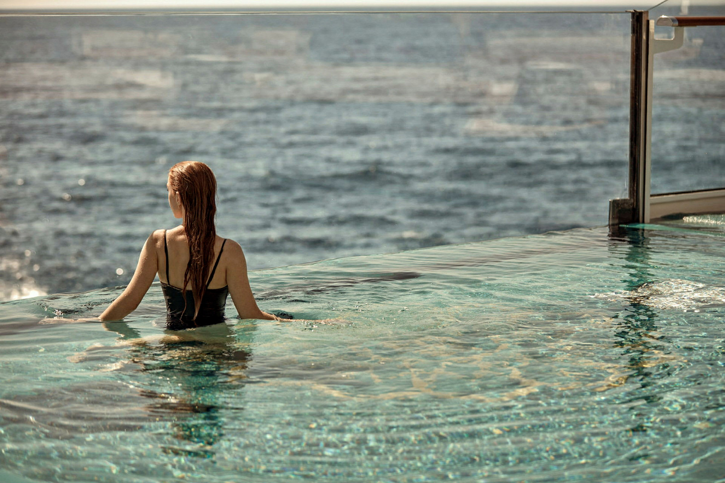En person sitter i en pool med utsikt över havet. (AI-genererad text)