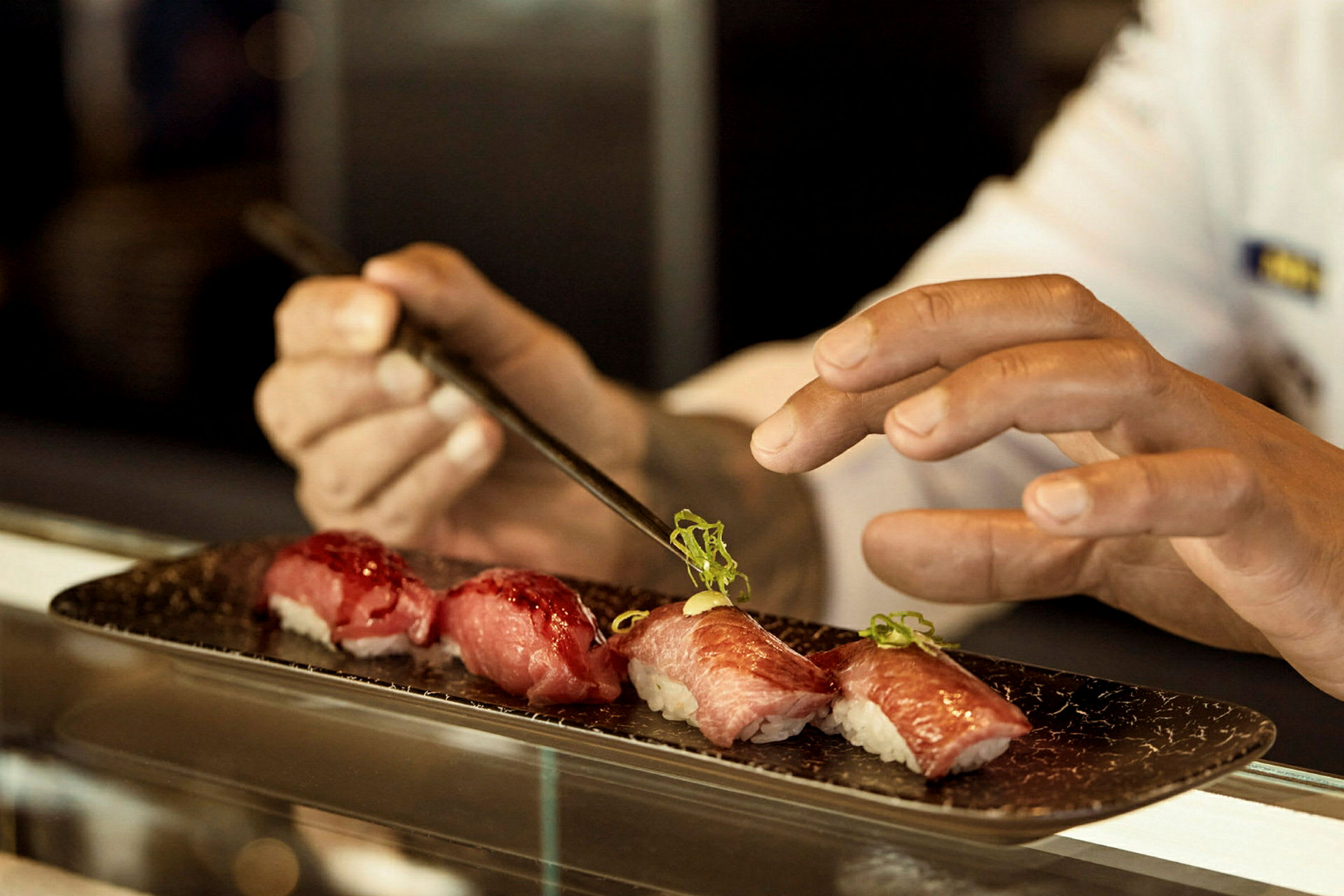 Närbild på en persons händer som placerar garnering ovanpå sushi. (AI-genererad text)
