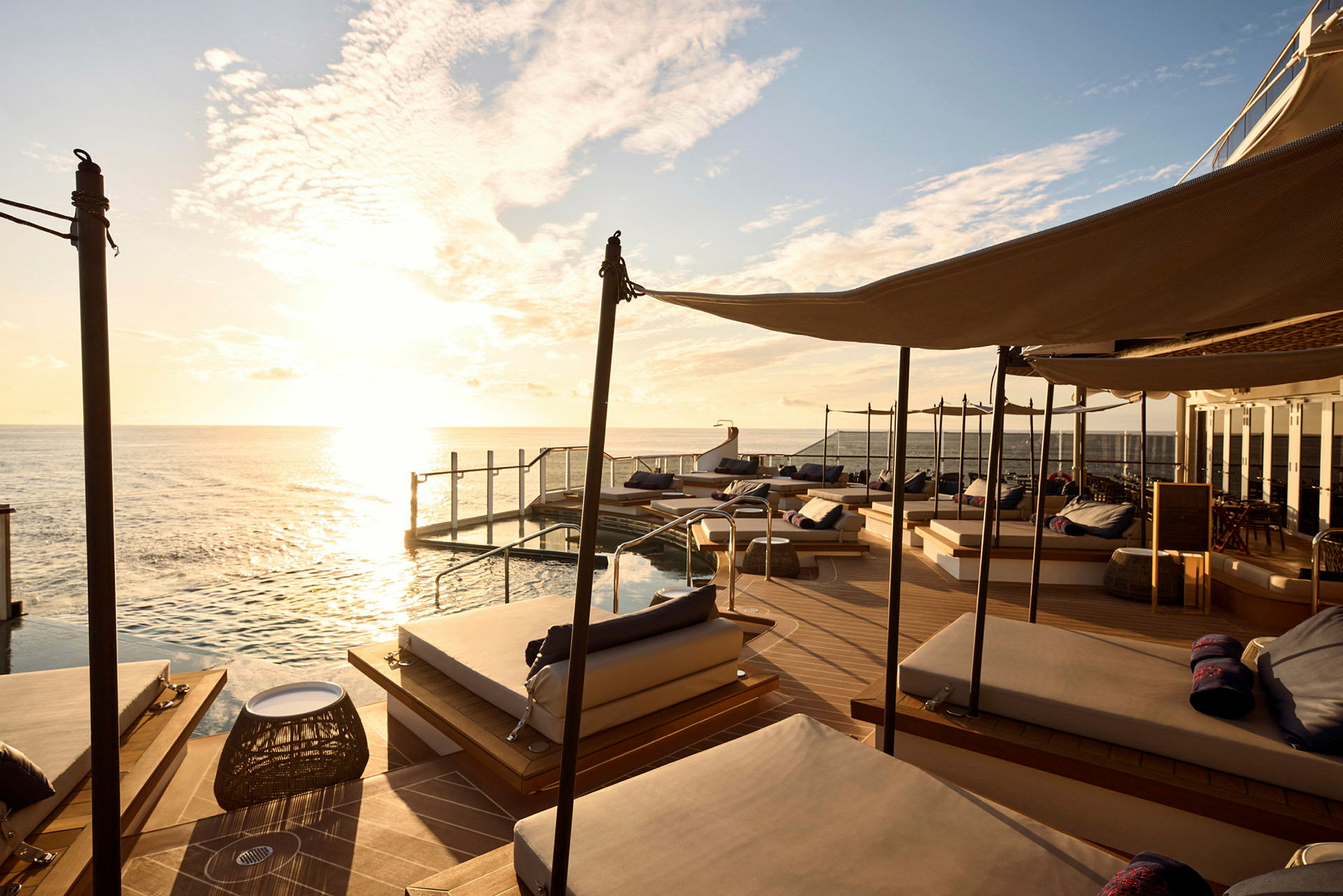 Solstolar vid en infinitypool med utsikt över havet under en solnedgång. (AI-genererad text)