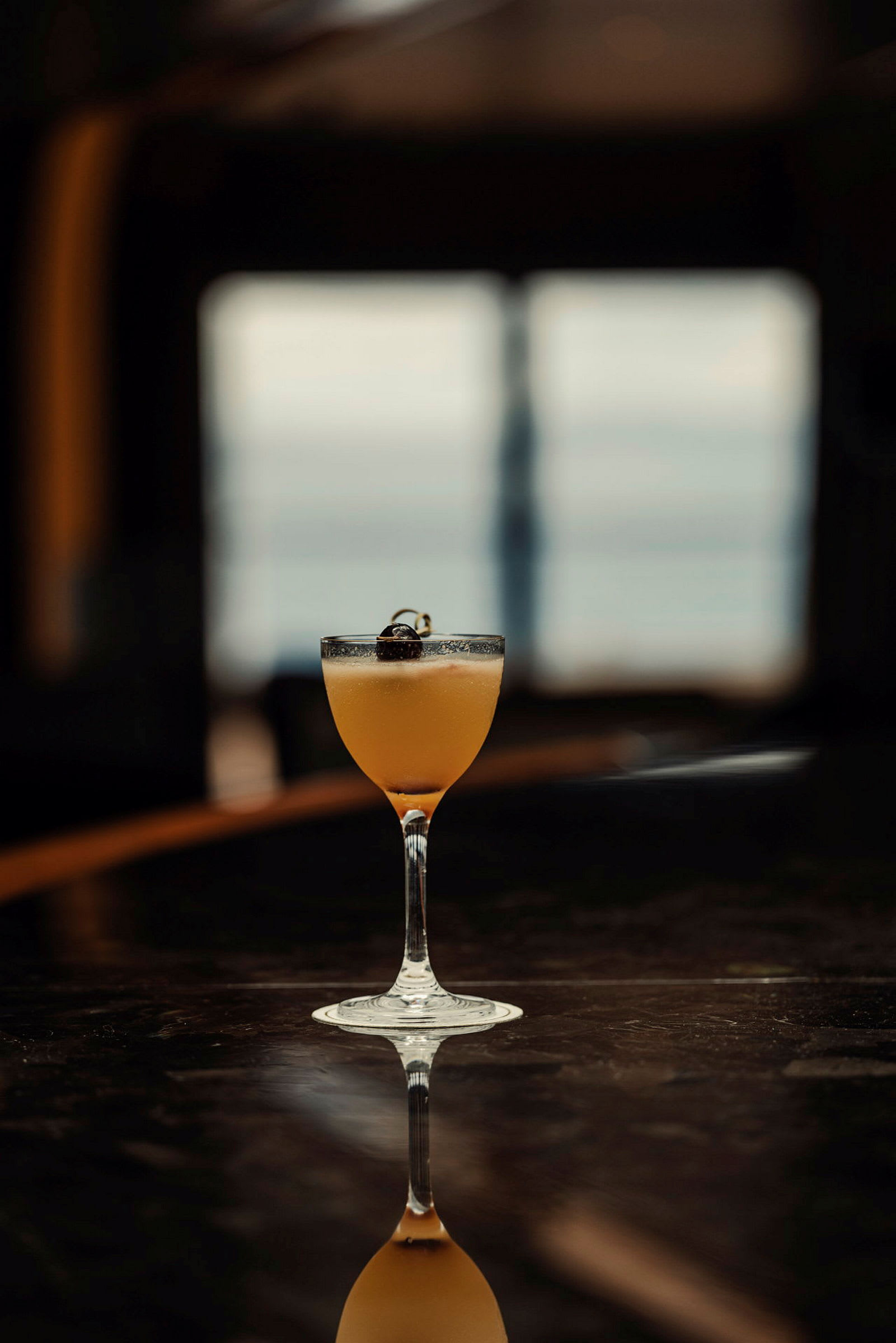 Ett glas med en orange drink prydd med ett körsbär på toppen. Glaset står på ett mörkt bord. (AI-genererad text)