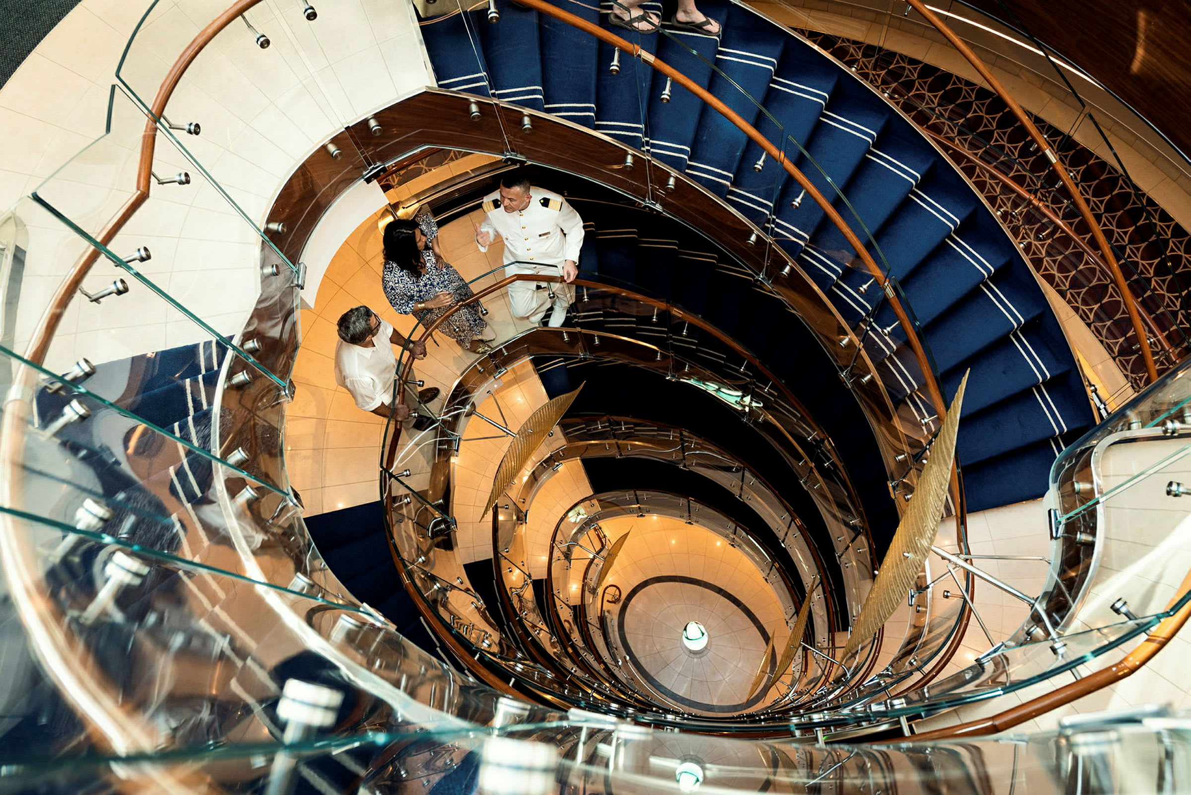 En spiraltrappa med glasräcken och blå stegmatta, fotograferad från ovan. (AI-genererad text)