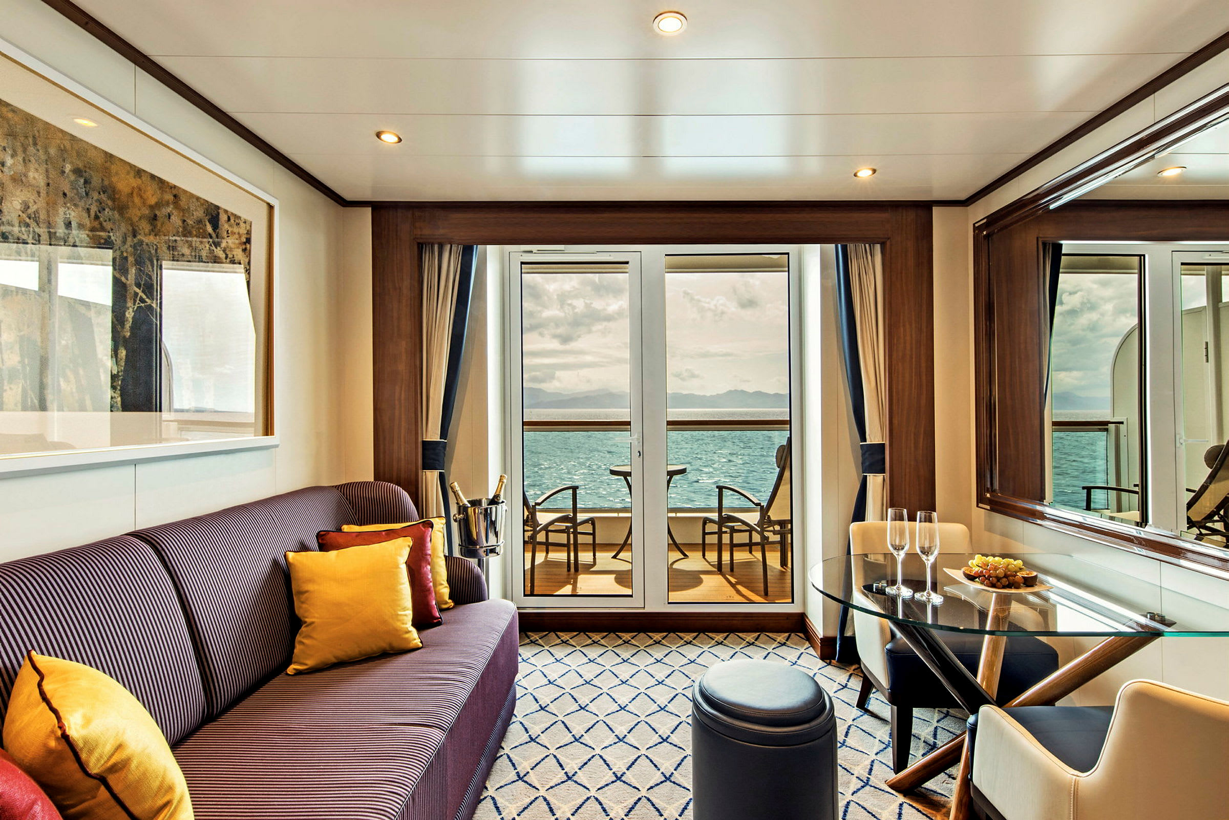 En elegant inredd rumsinteriör med en soffa, bord, och stolar samt en utsikt mot havet från en veranda. (AI-genererad text)