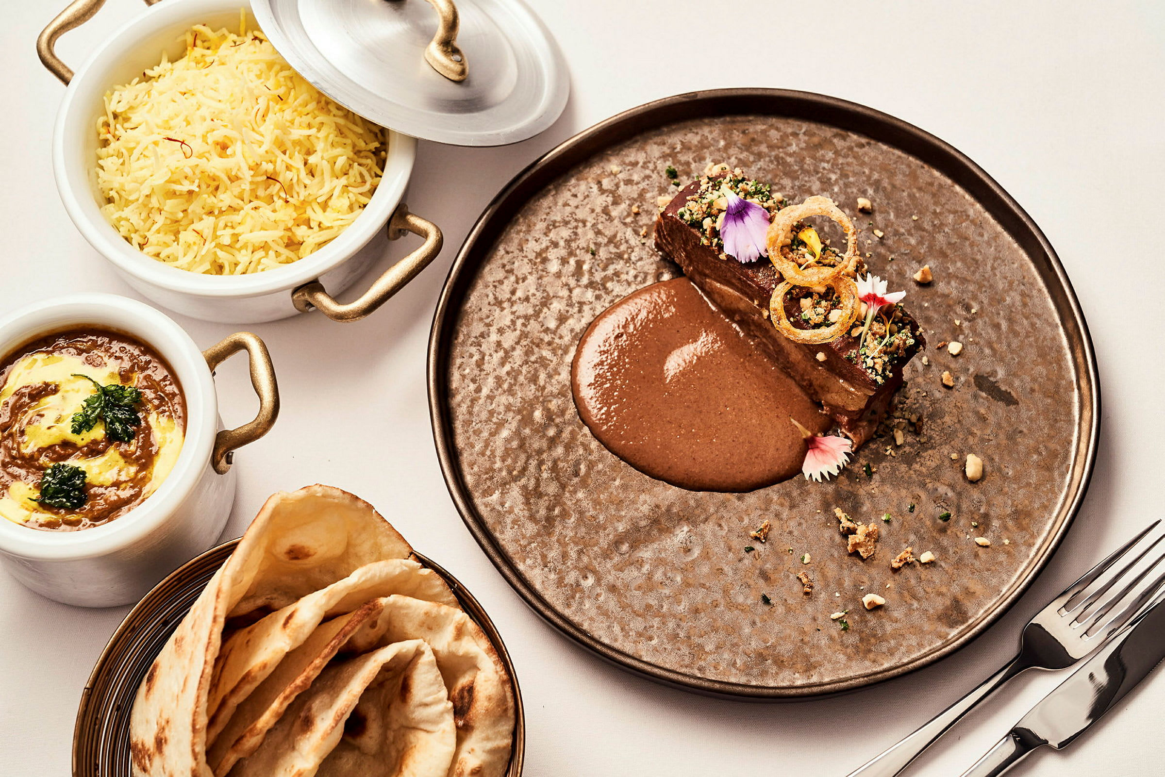 Tallrik med en köttbit och sås, bröd och skål med ris samt gryta. (AI-genererad text)