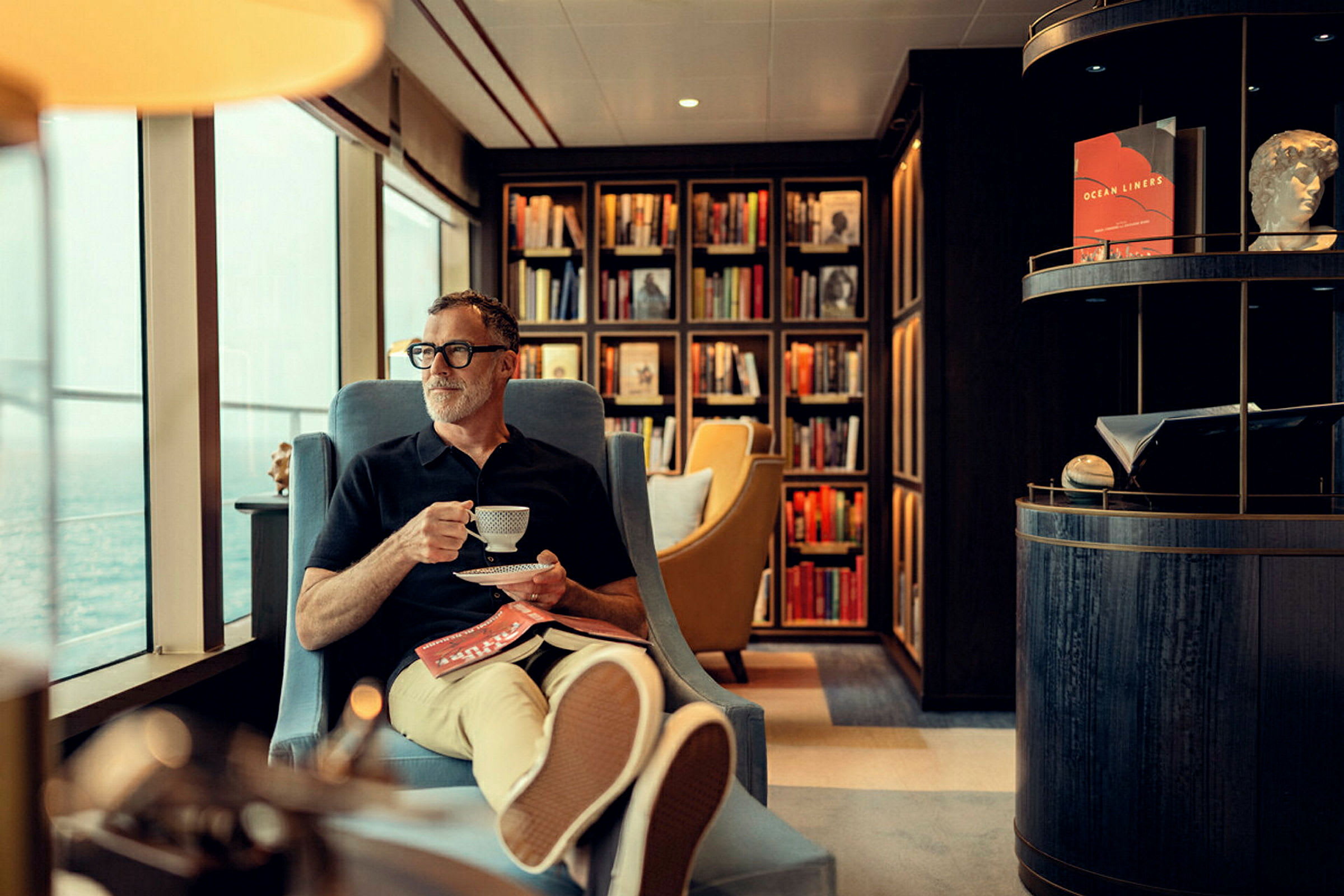 En person sitter bekvämt i en fåtölj med en kopp kaffe framför en bokhylla fylld med böcker. (AI-genererad text)