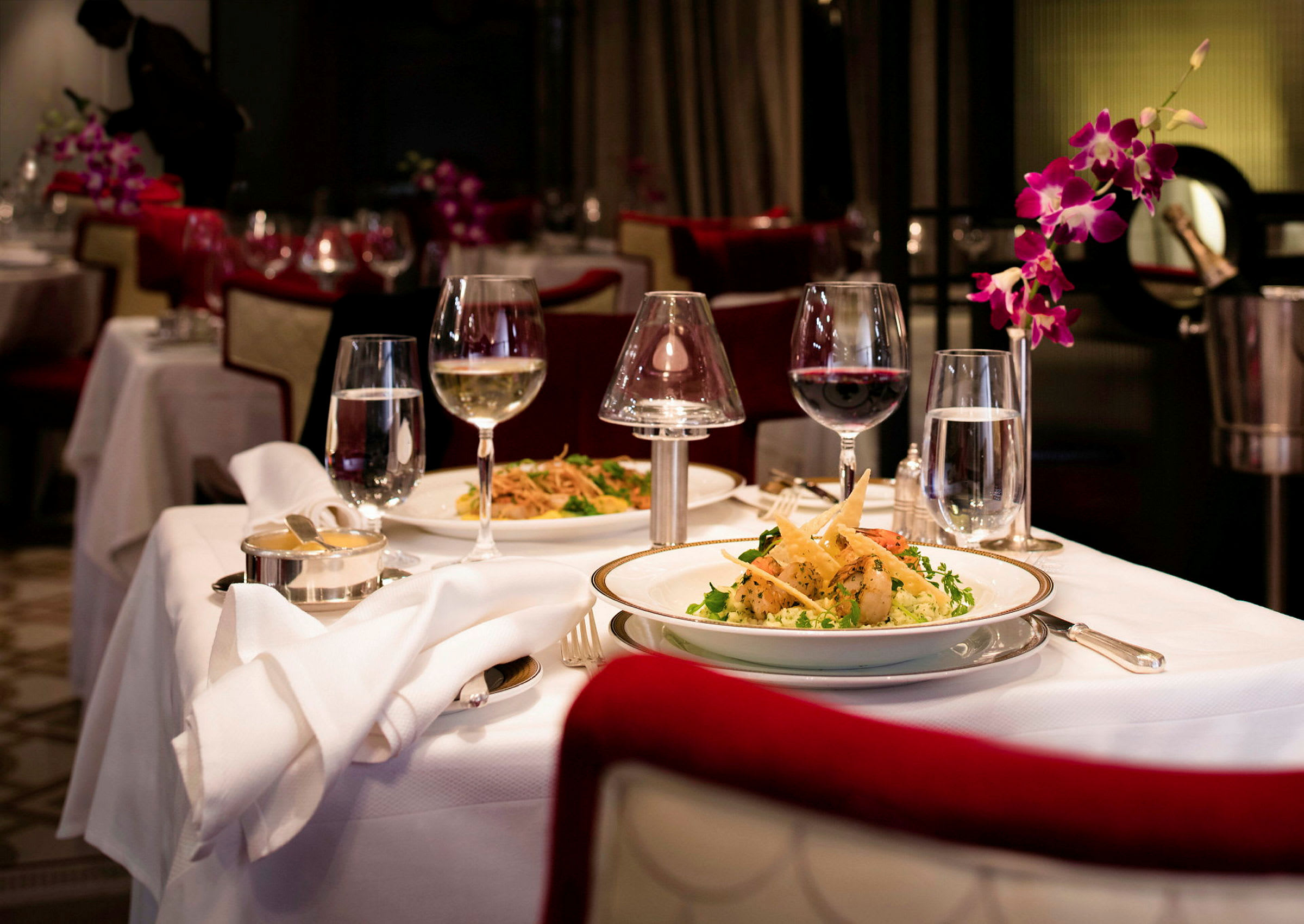Ett uppdukat restaurangbord med mat, glas med vin och vatten, samt blommor som dekoration. (AI-genererad text)