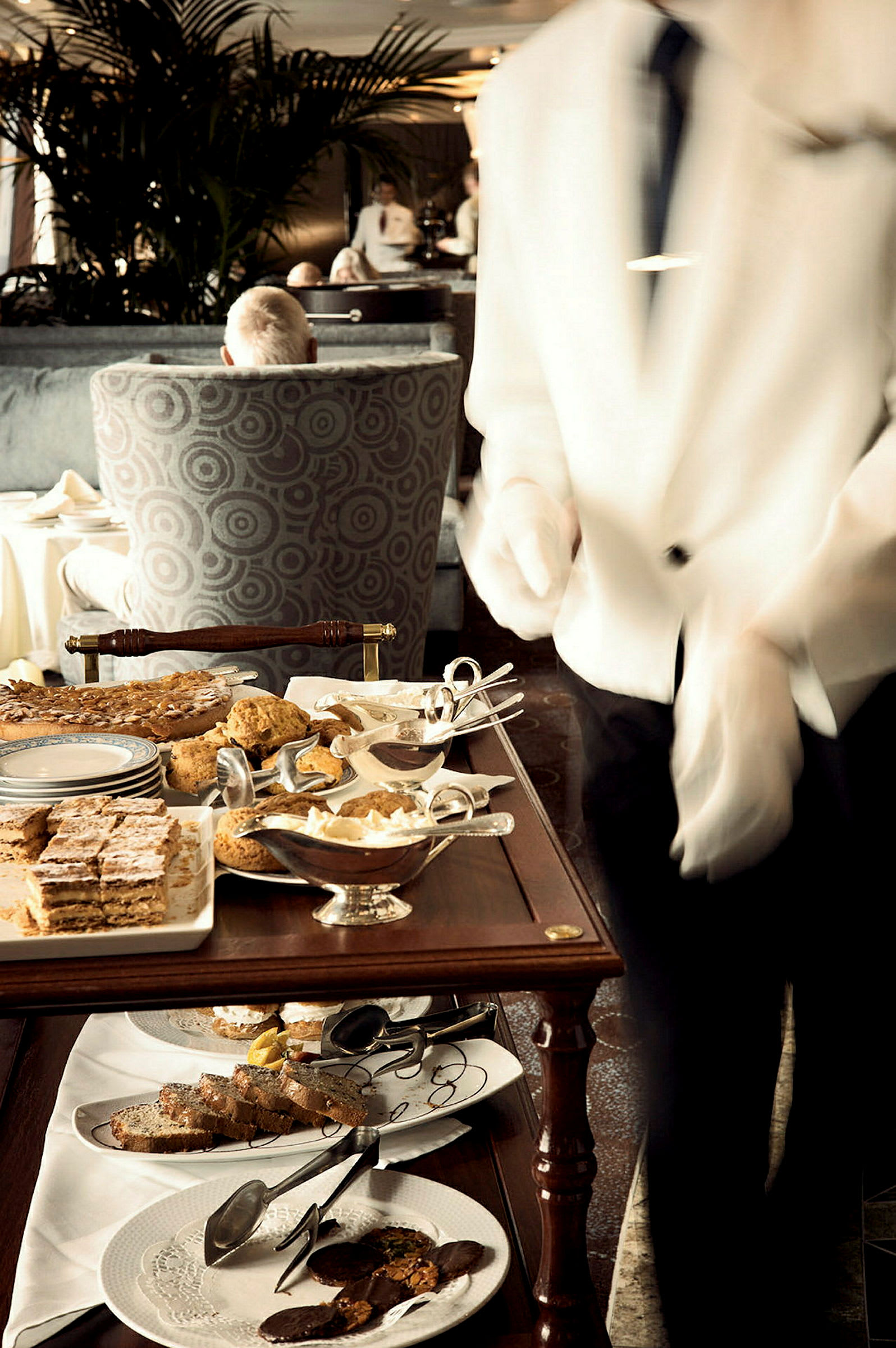 En serveringsvagn fylld med olika bakverk och desserter, omgiven av en elegant miljö med bekväma sittplatser. (AI-genererad text)