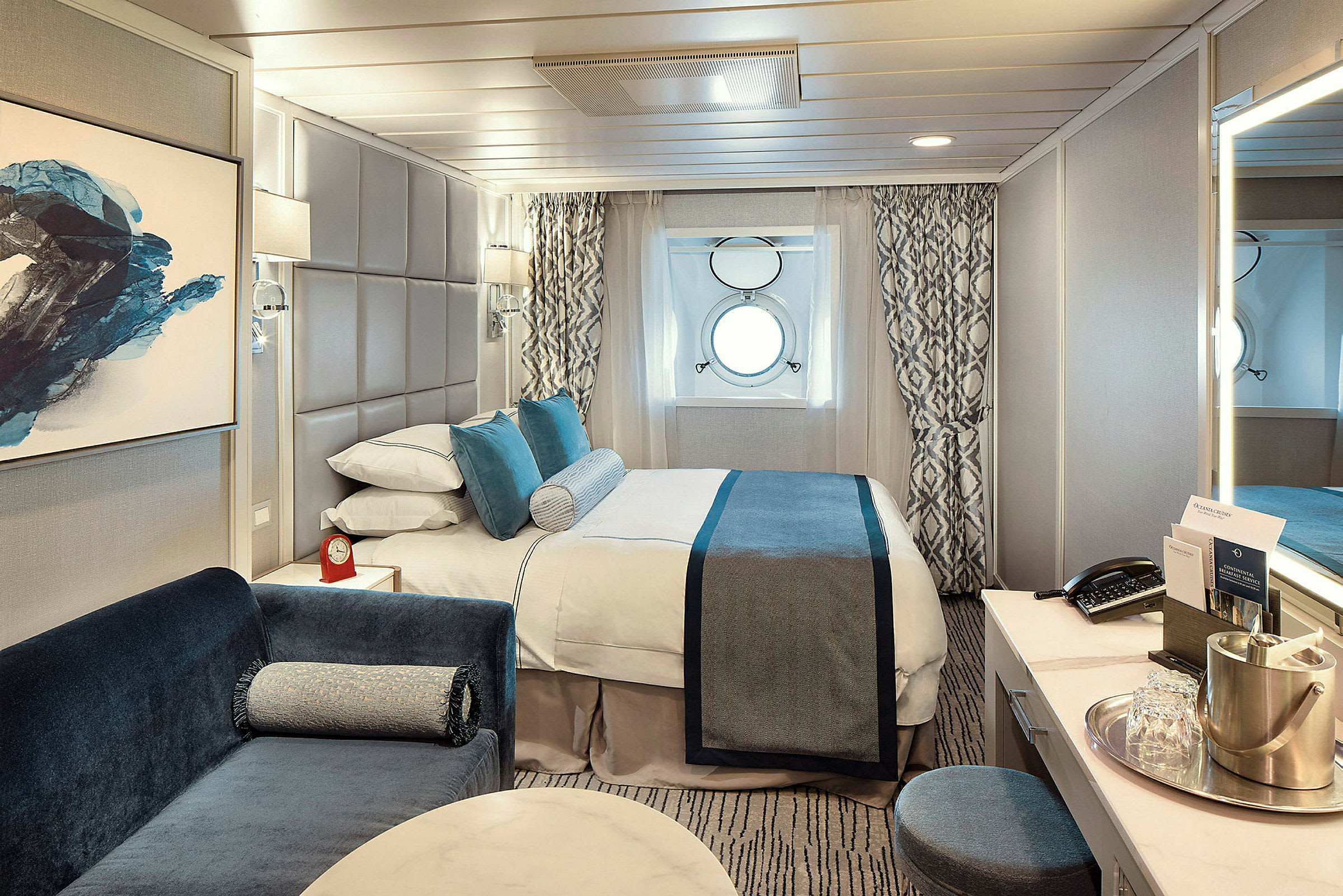 En elegant designad hytt med en dubbelsäng, två små runda fönster och en soffa intill sängen. (AI-genererad text)