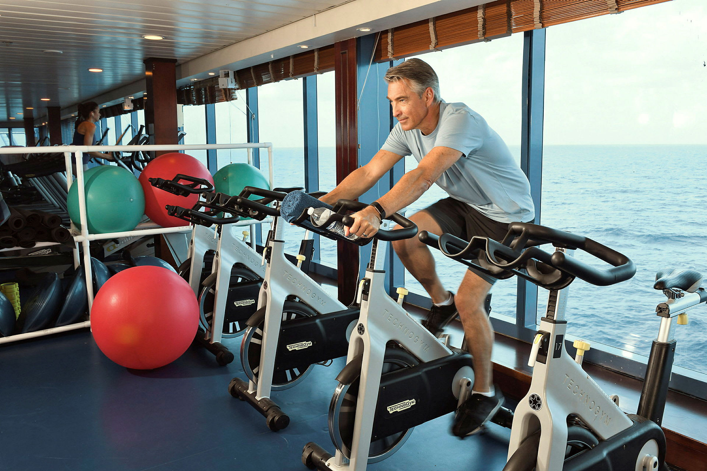 En person tränar på en spinningcykel i ett gym med havsutsikt. (AI-genererad text)