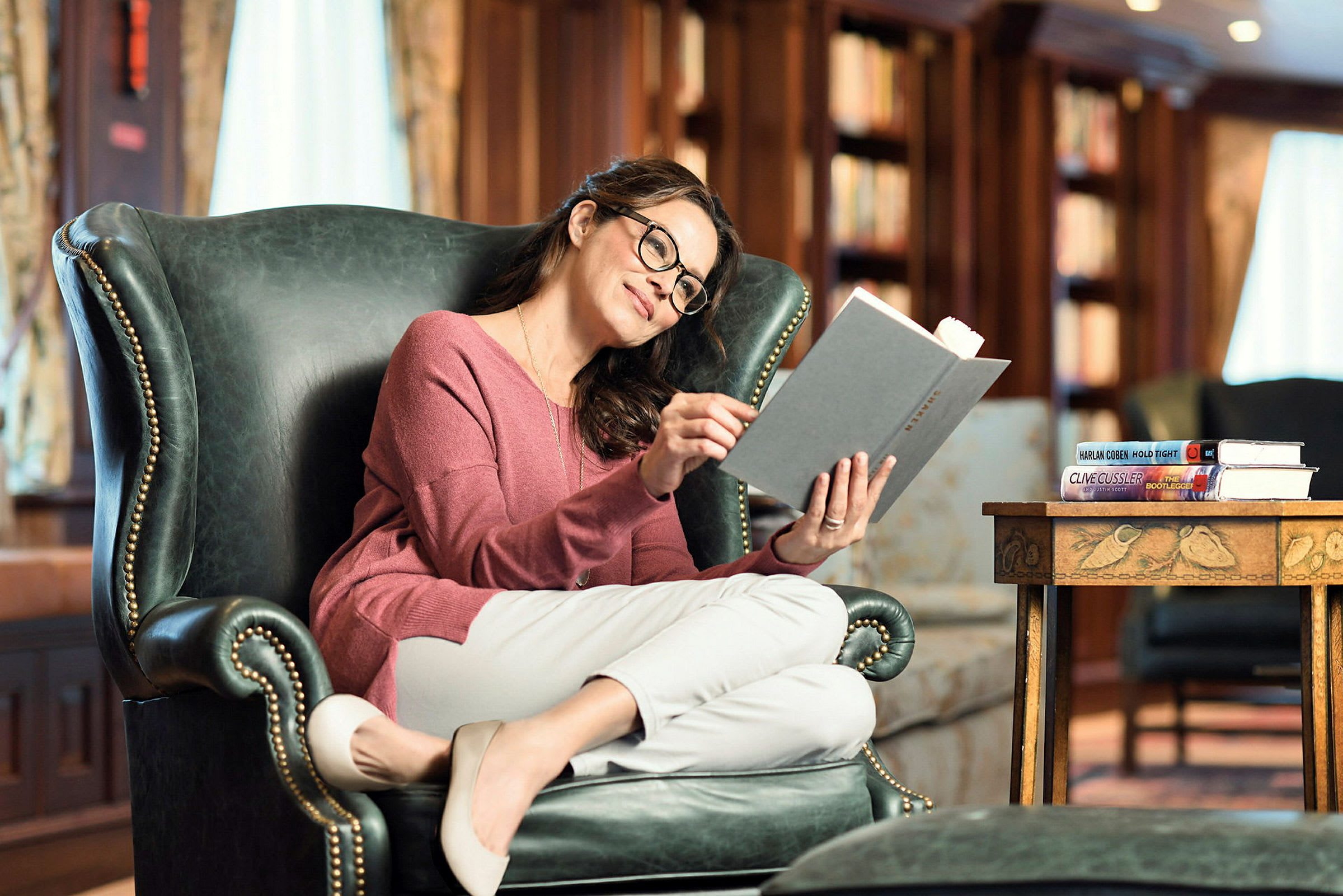 Person sitter i en fåtölj och läser en bok, med bokhyllor i bakgrunden. (AI-genererad text)