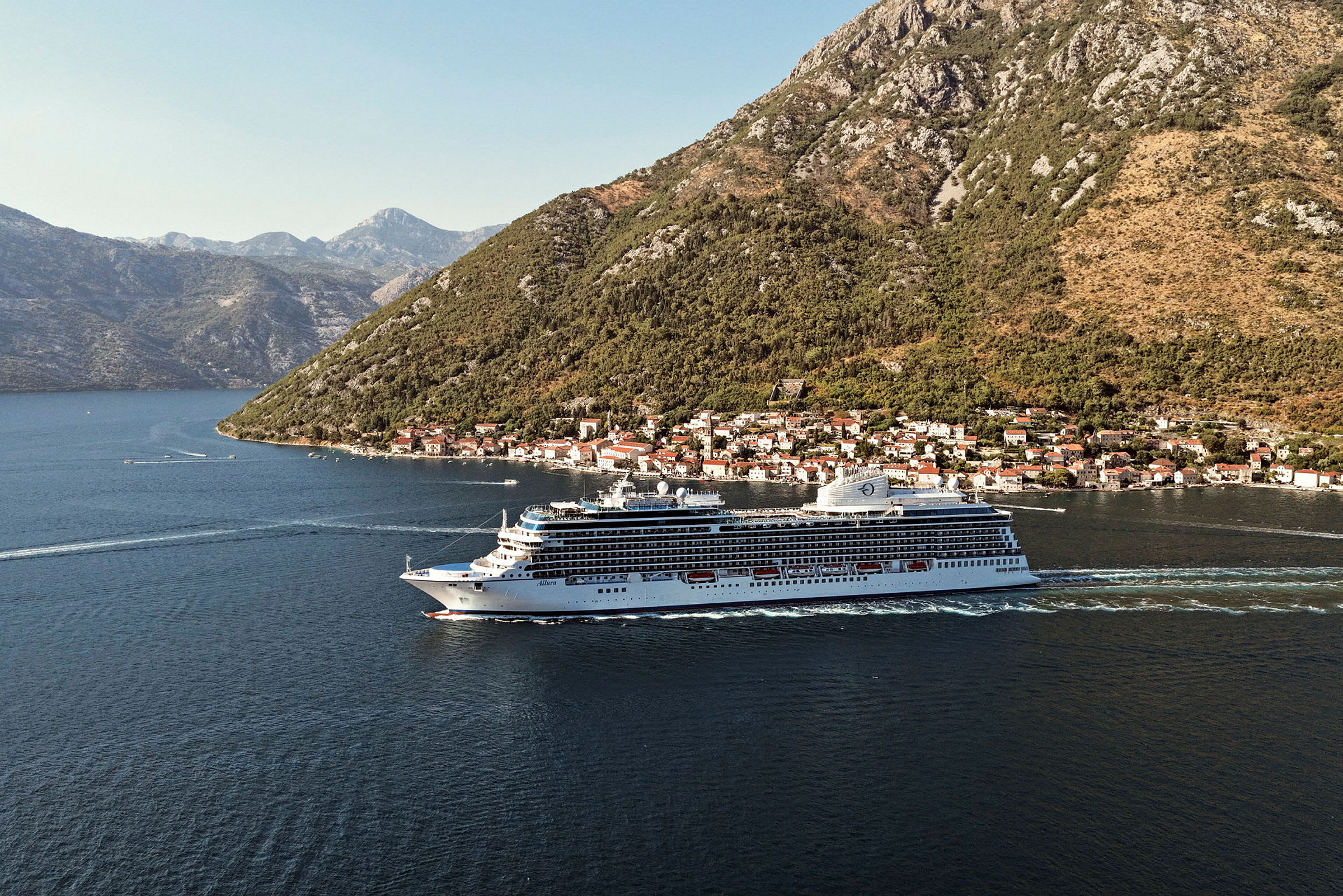 Ett kryssningsfartyg seglar i en fjord med berg och en by i bakgrunden. (AI-genererad text)