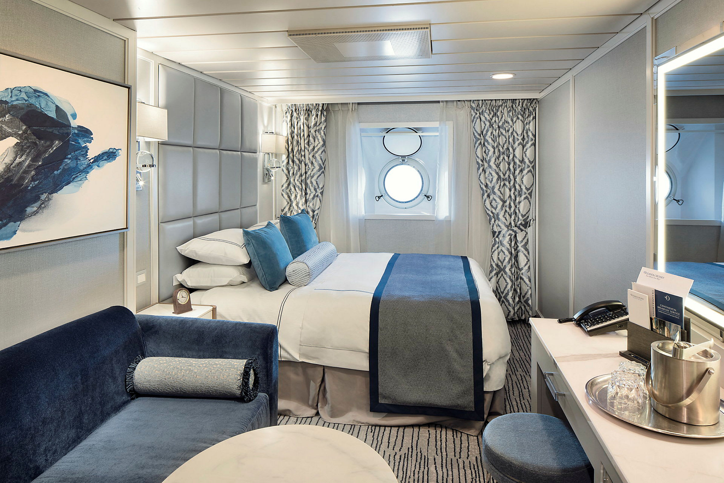Ett hotellrum inrett med en säng, blå dekor och ett runt fönster. (AI-genererad text)