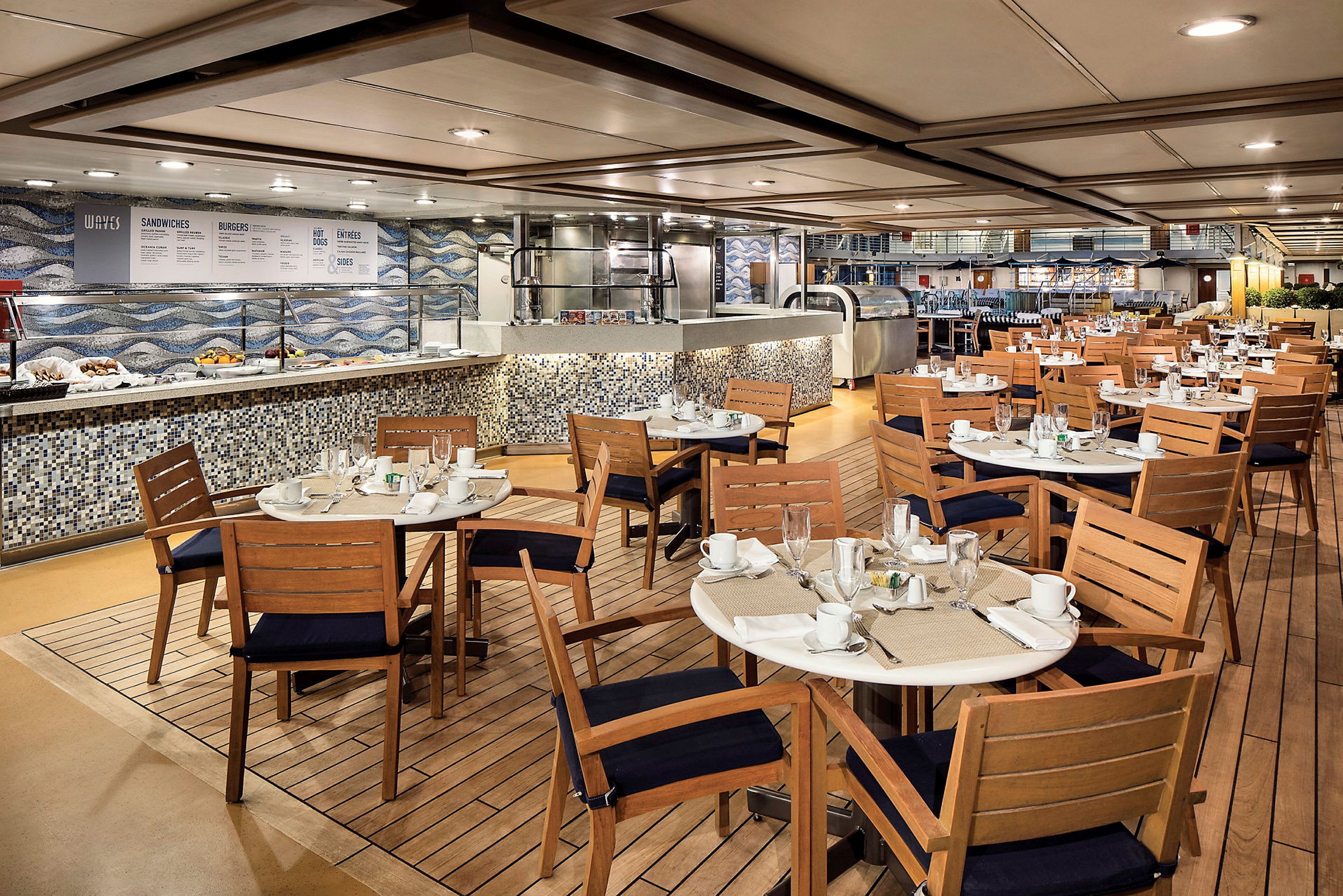 En restaurang med träbord och stolar, dukade för middag. I bakgrunden finns en matservering med mosaikkakel. (AI-genererad text)