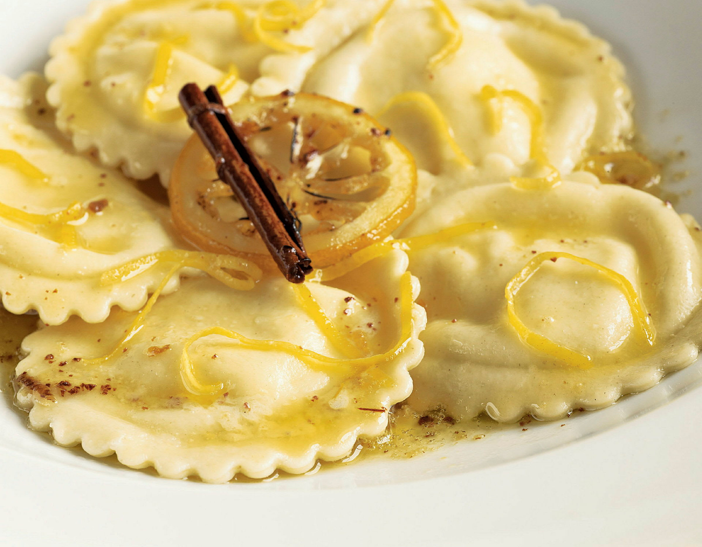Ett fat med ravioli toppat med citronskal och en kanelstång. (AI-genererad text)