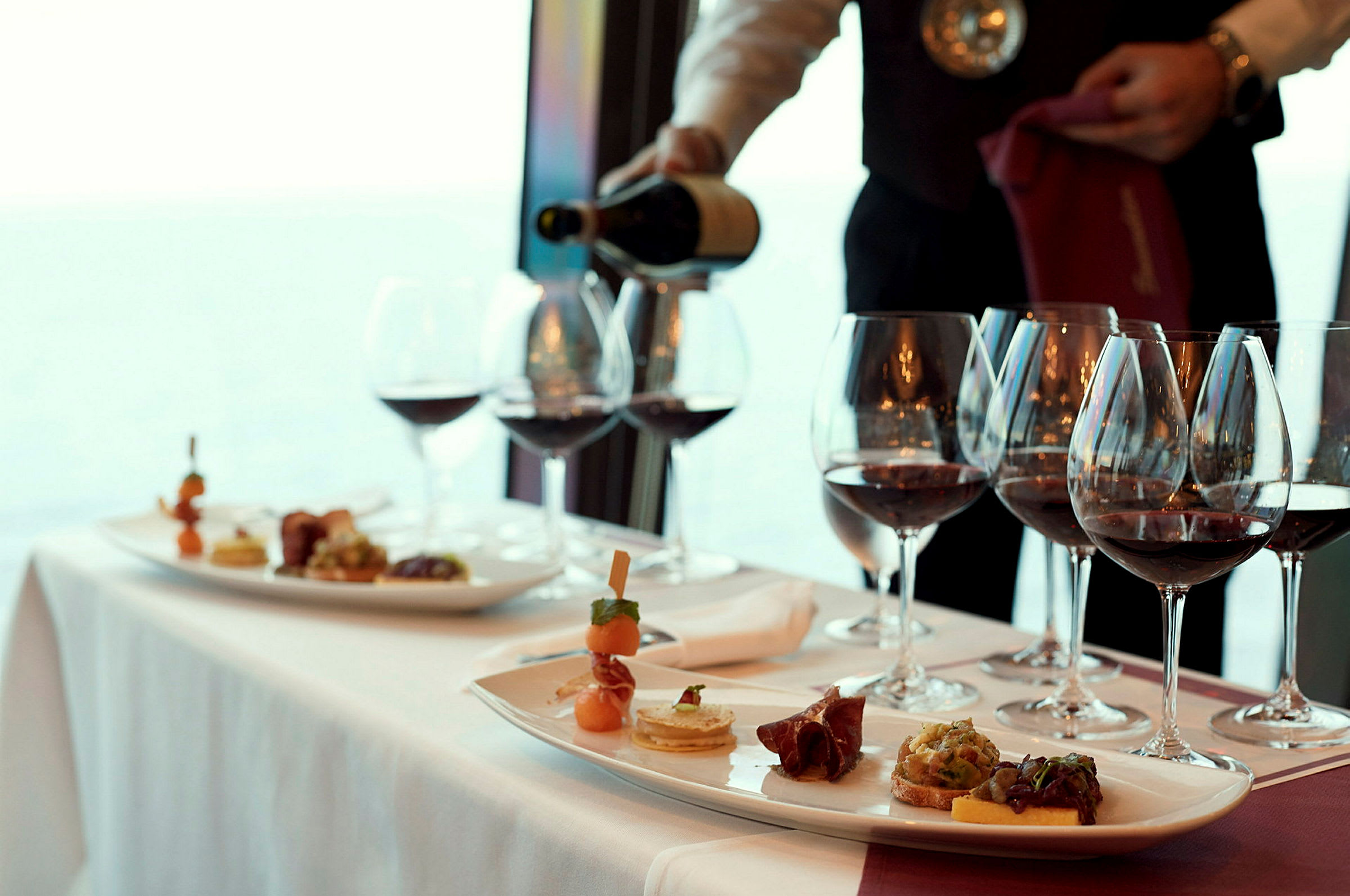 Servitör häller vin i glas på ett dukat bord. (AI-genererad text)