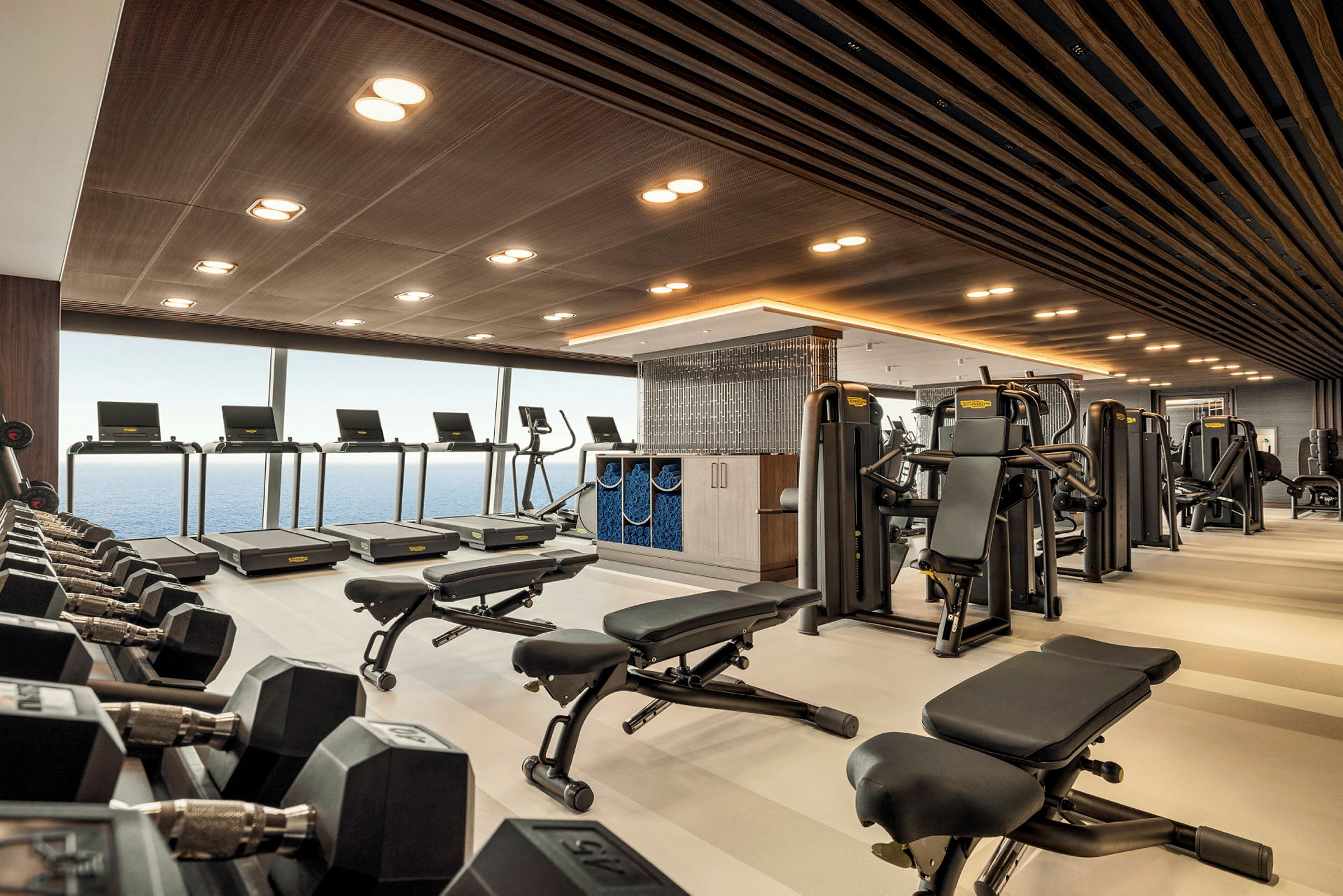 Gym med träningsmaskiner, träningsbänkar och löpband samt fönster med havsutsikt. (AI-genererad text)