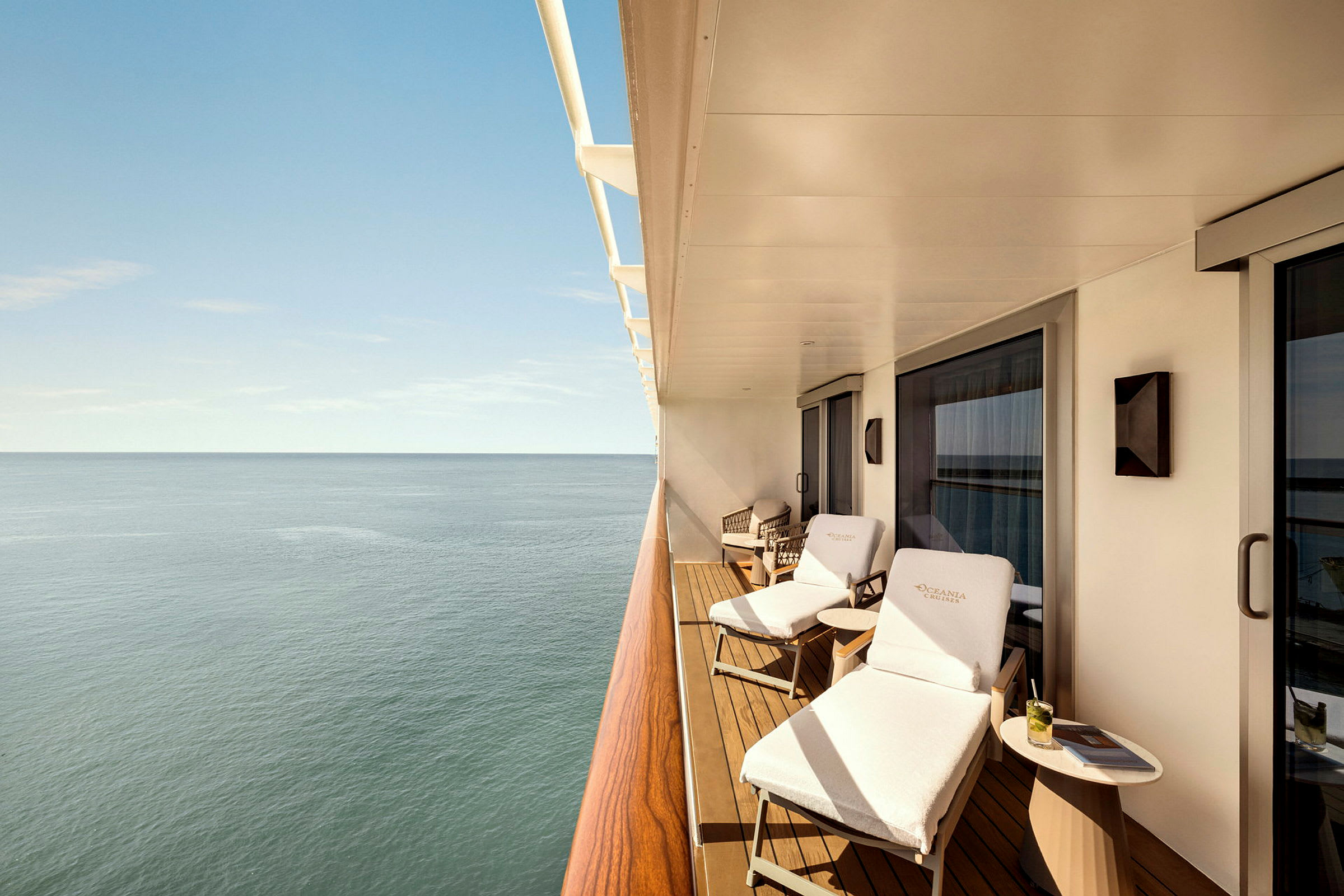 Utsikt från en balkong med solstolar och ett bord, över havet under klar himmel. (AI-genererad text)