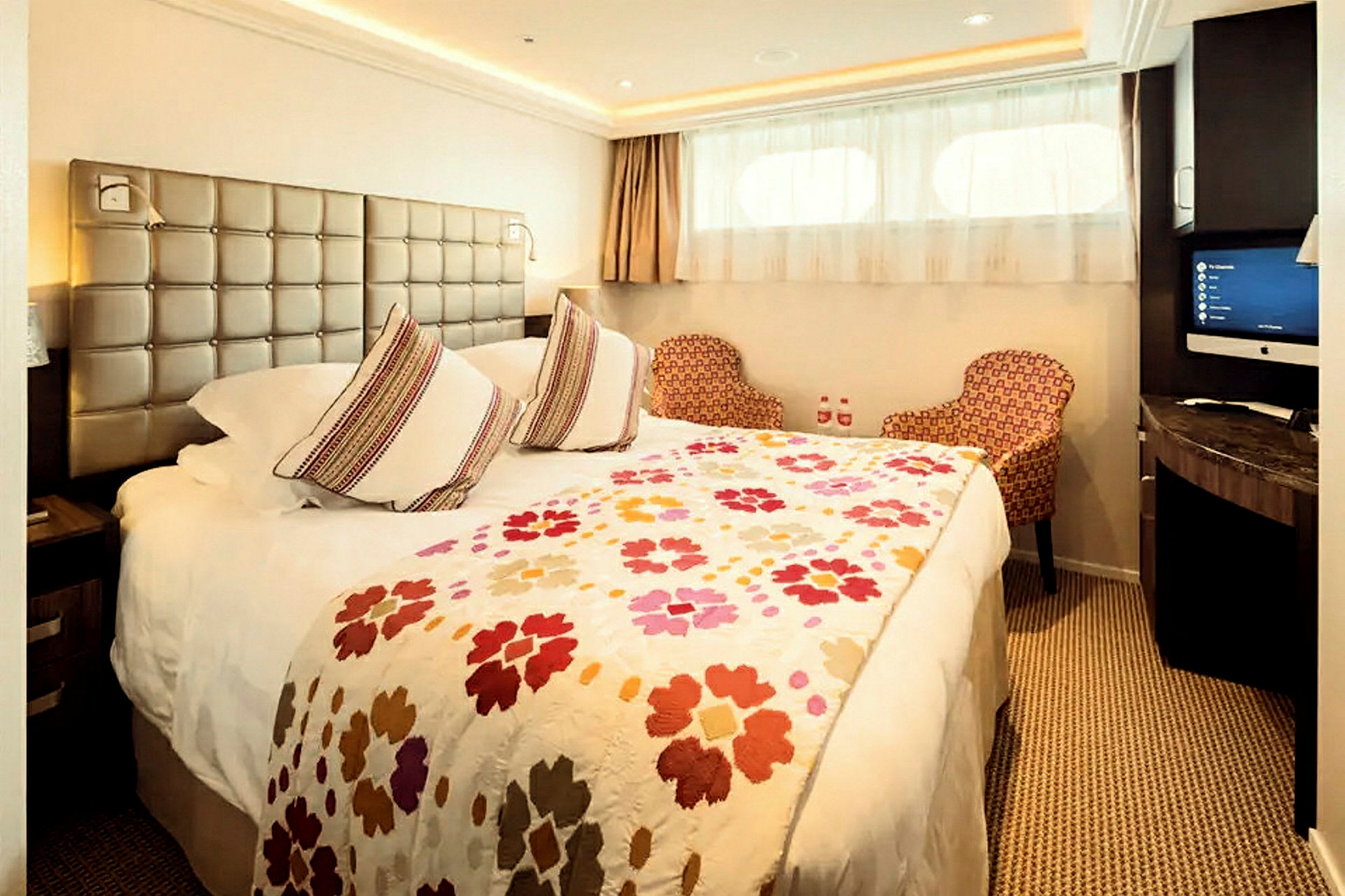 Ett hotellrum med en stor säng, två dekorativa stolar och en väggmonterad TV. (AI-genererad text)