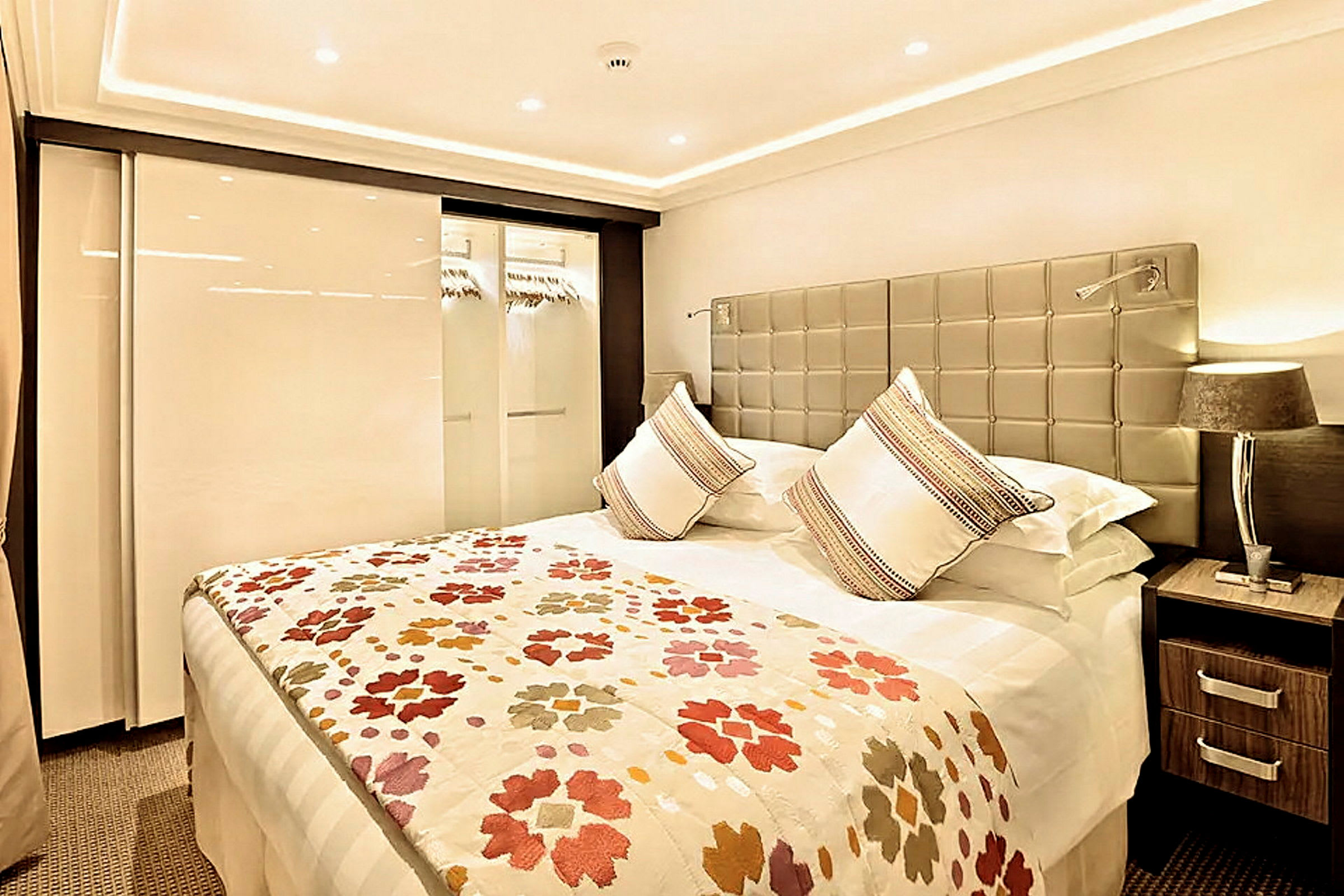 Modernt sovrum med en stor säng, dekorativa kuddar och ett färgglatt täcke. (AI-genererad text)