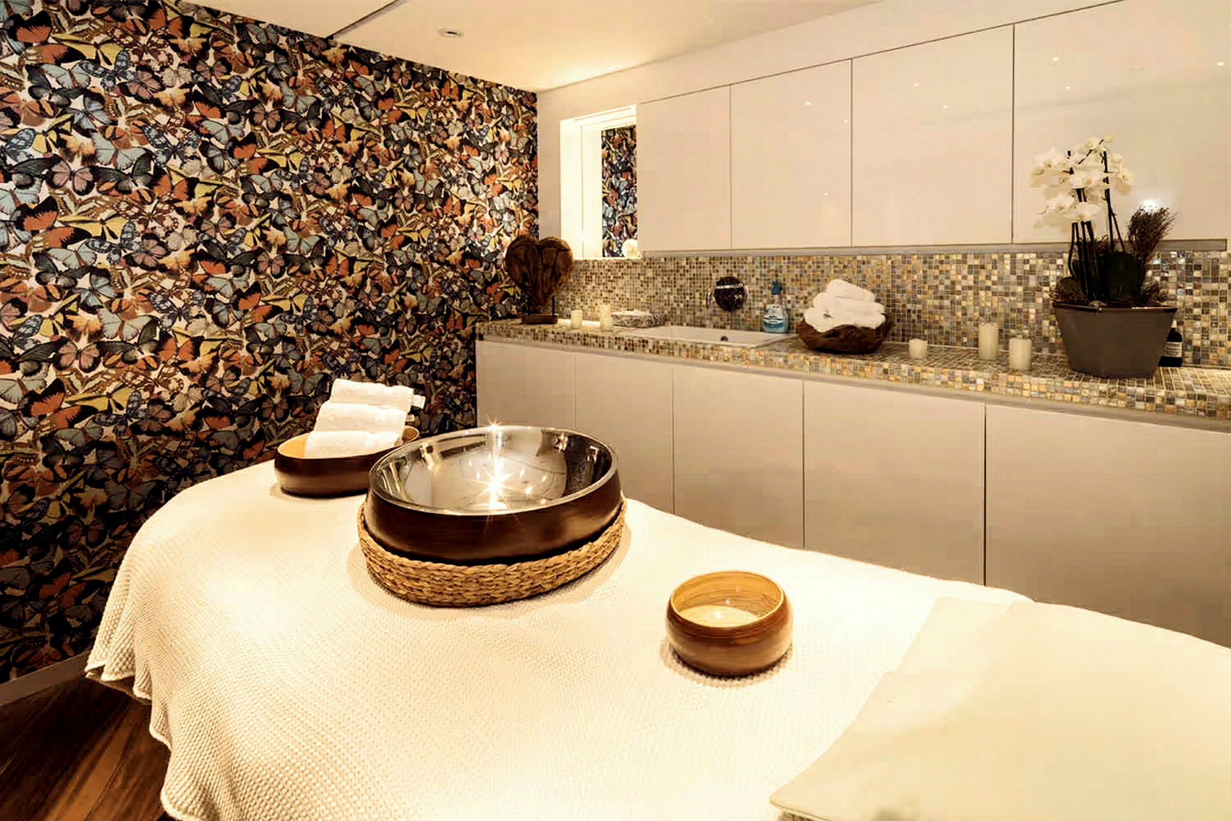 Ett massagebord i ett rum med mosaikdekorer och blommande växter. (AI-genererad text)