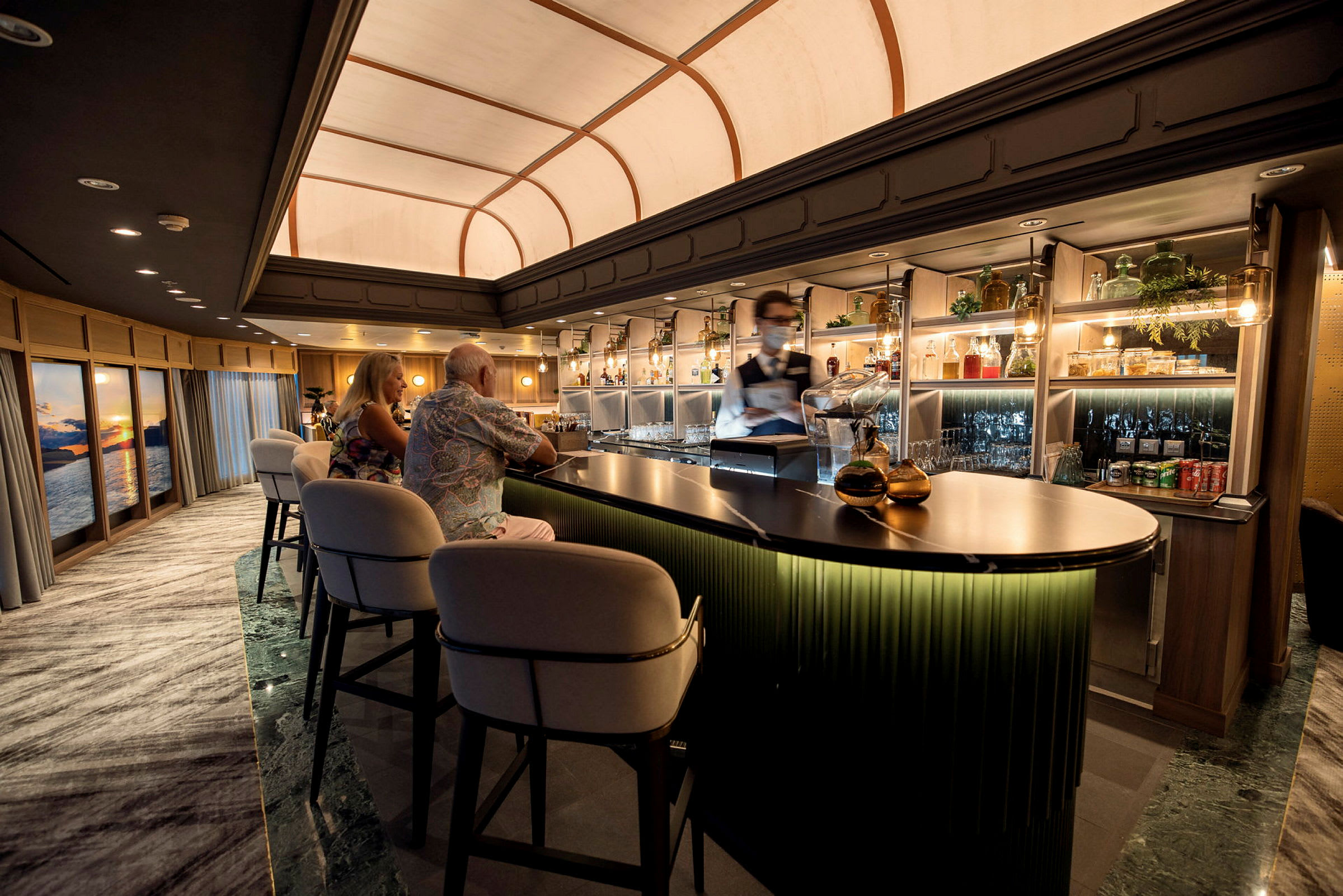 En elegant bar med bekväma barstolar, hyllor med flaskor och glas samt en varm belysning. (AI-genererad text)