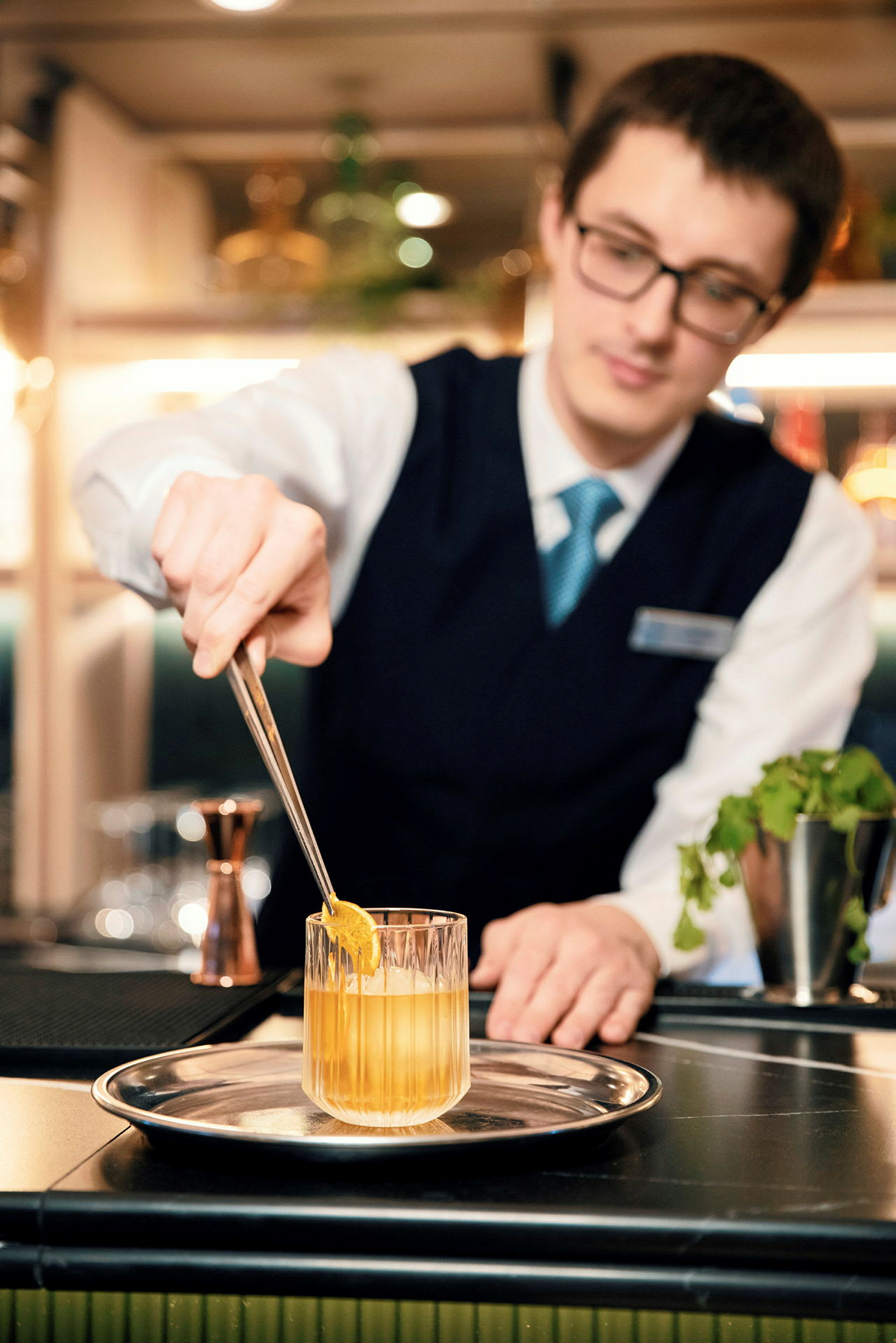 En glasdrink med en orange dekoration placeras på en silverbricka. (AI-genererad text)