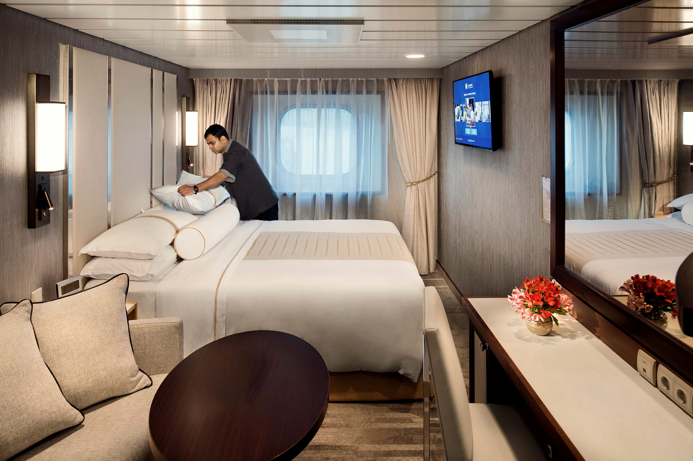 Interiör av ett hotellrum med en säng, bord, soffa och spegel. (AI-genererad text)