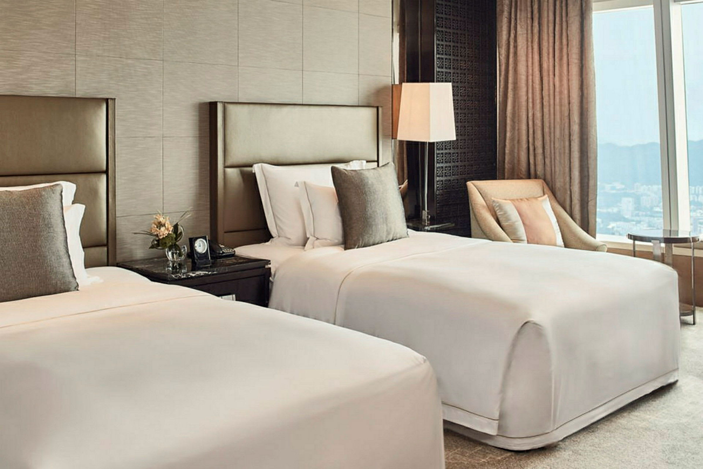 Ett hotellrum med två enkelsängar, nattduksbord, en fåtölj och ett stort fönster med utsikt. (AI-genererad text)