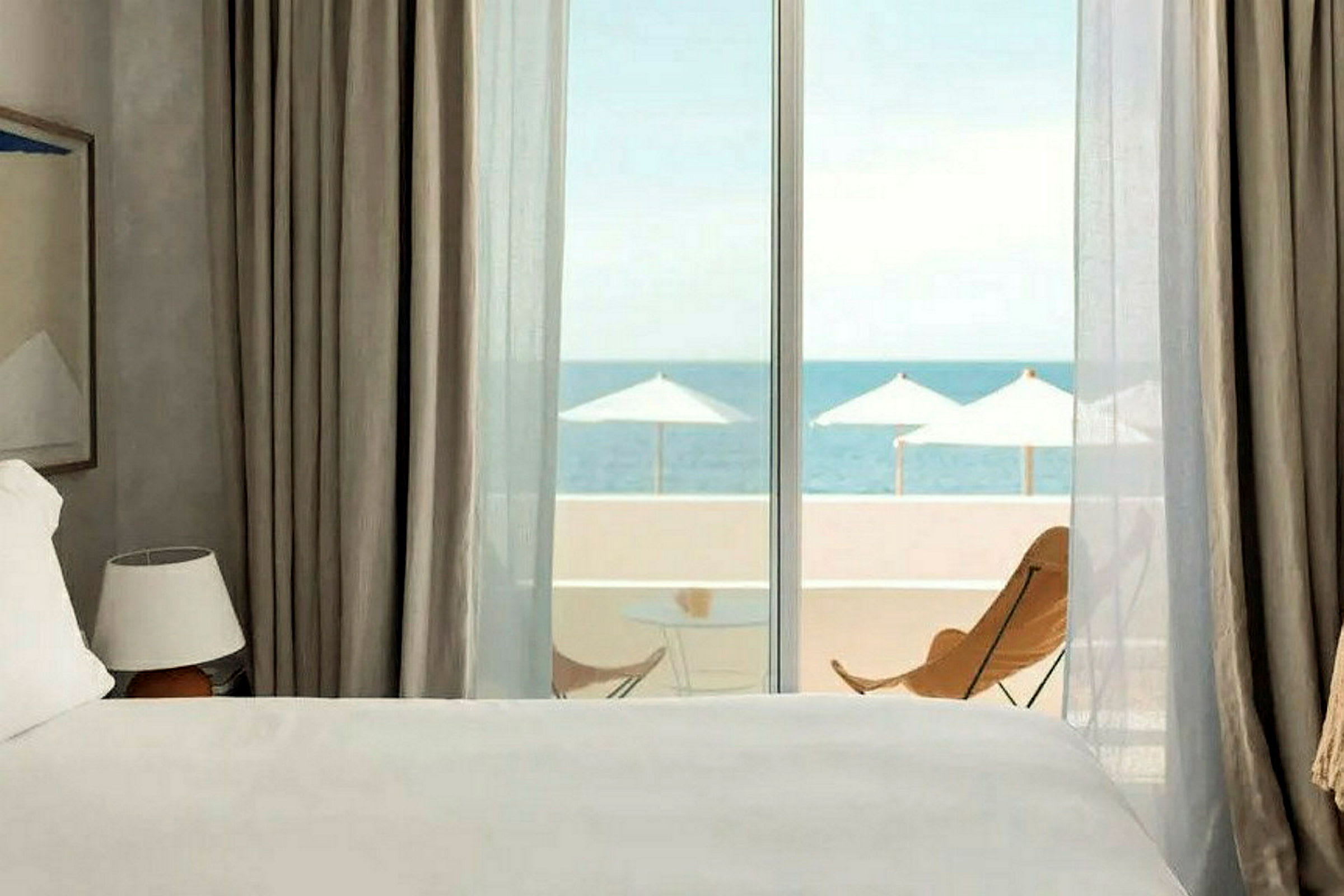 Ett hotellrum med havsutsikt genom en glasdörr, säng i förgrunden. (AI-genererad text)